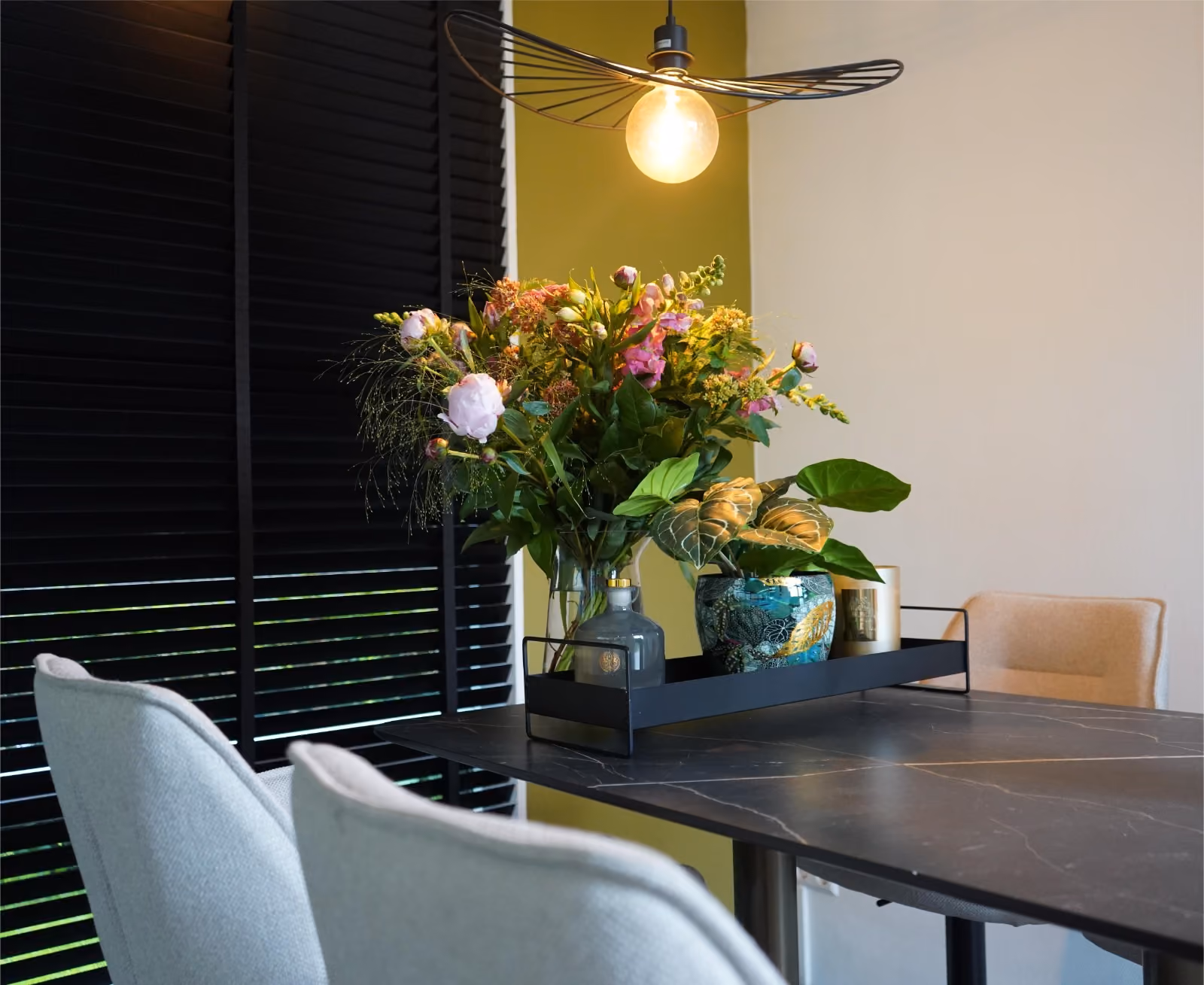 Modern dining table with a black tray holding floral arrangements under a glowing pendant light.