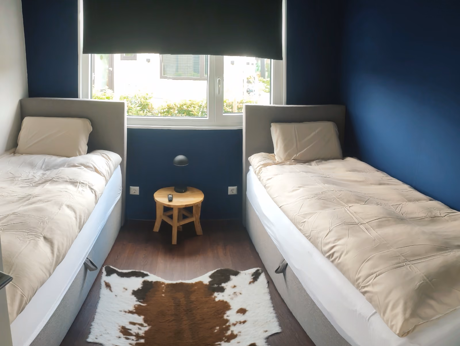 Minimalist bedroom with two single beds, a wooden stool nightstand, and a cowhide rug.