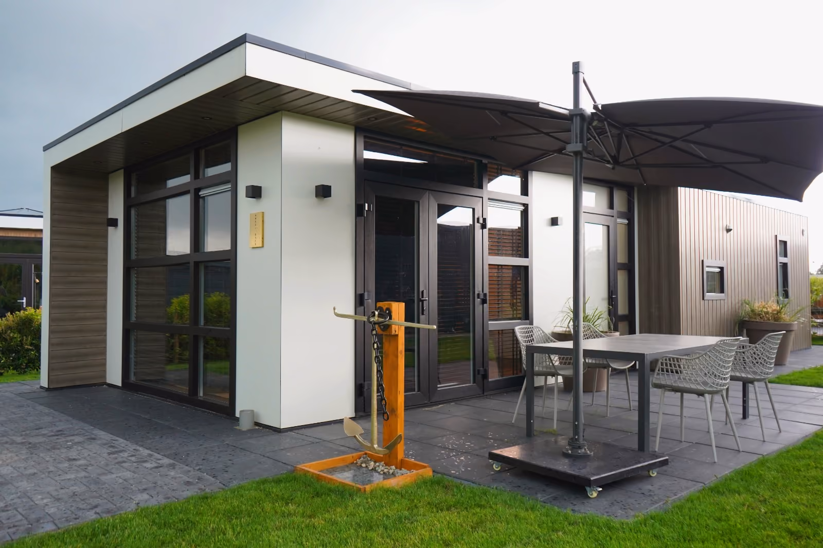 Modern patio with table, chairs, large umbrella, and a metal anchor decoration near glass doors.