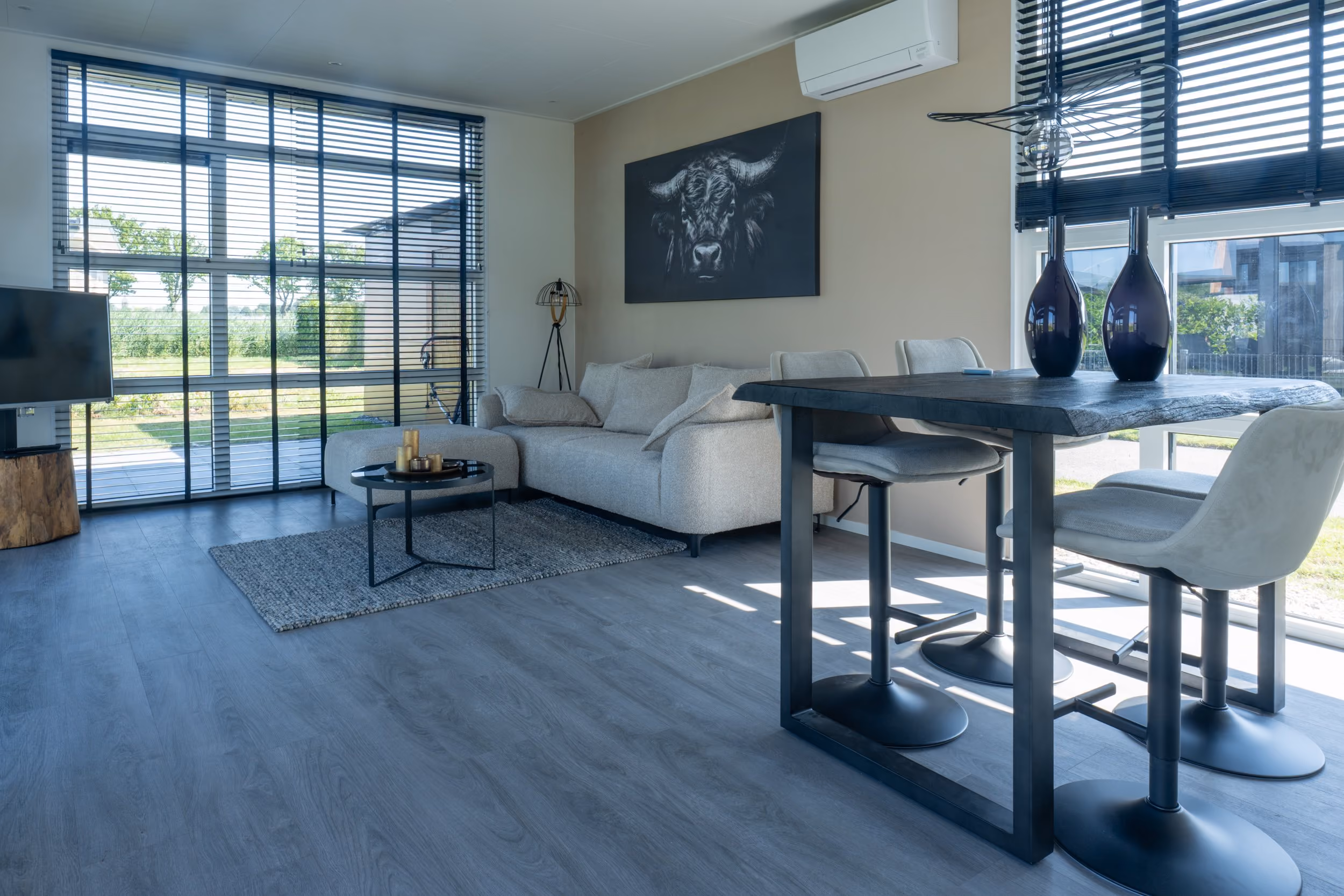 Modern living room with large windows, beige sofa, black coffee table, and dining table with chairs.