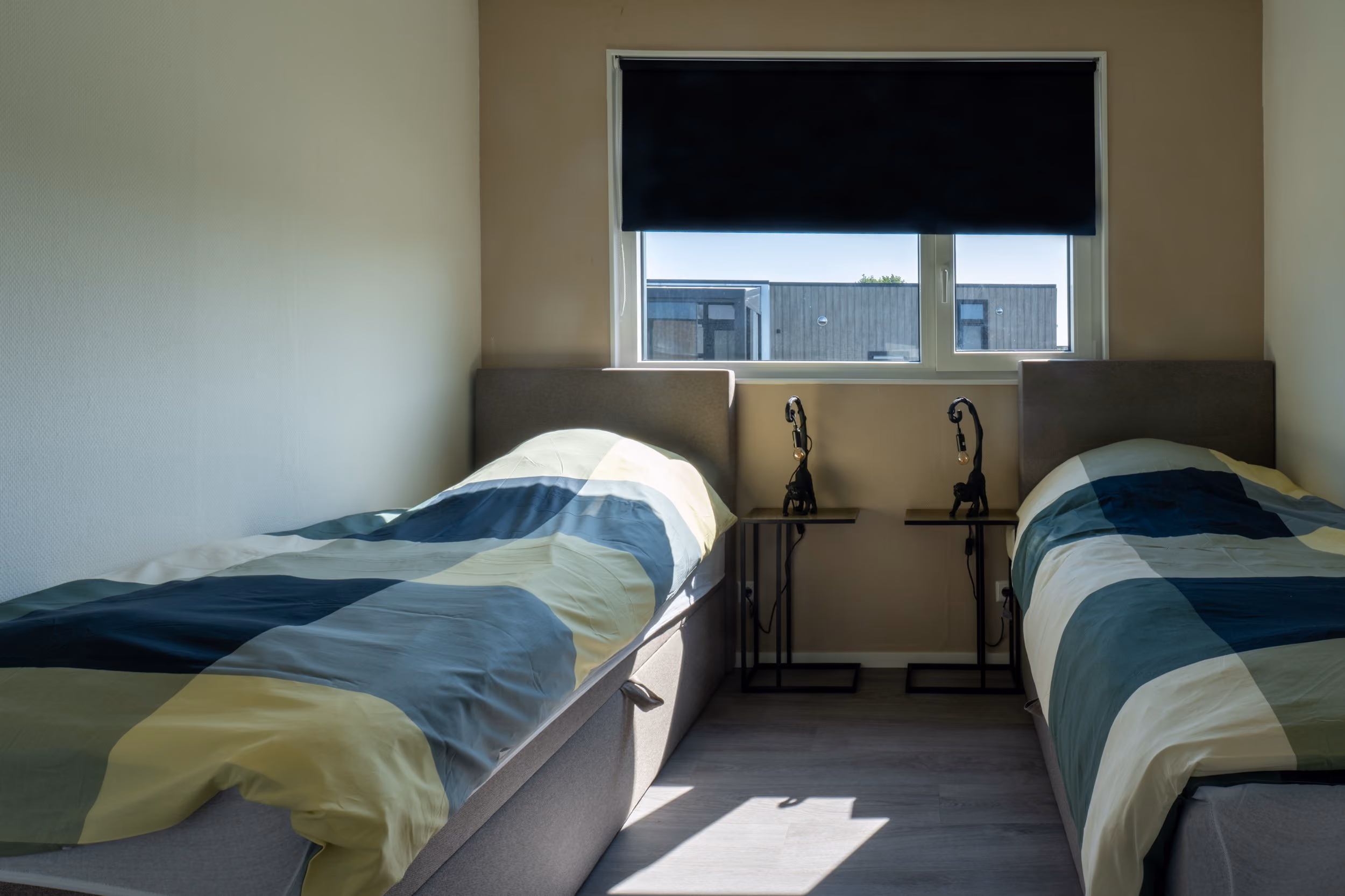 Room with two single beds with striped bedding and a window with a black blind.