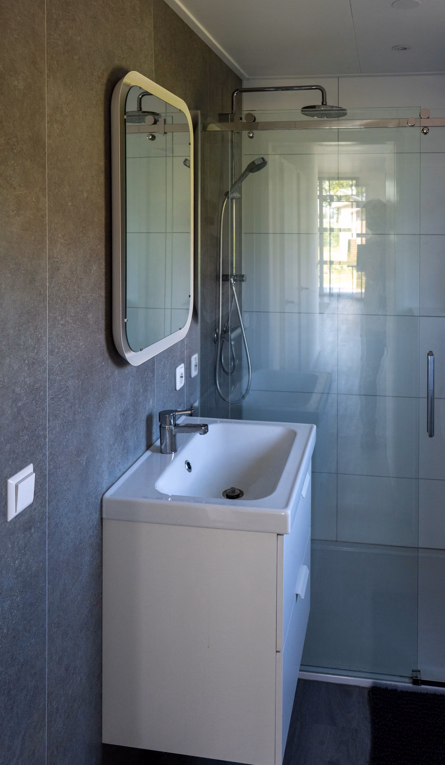 Minimalist bathroom with white sink cabinet, wall mirror, and glass shower enclosure with rain showerhead.
