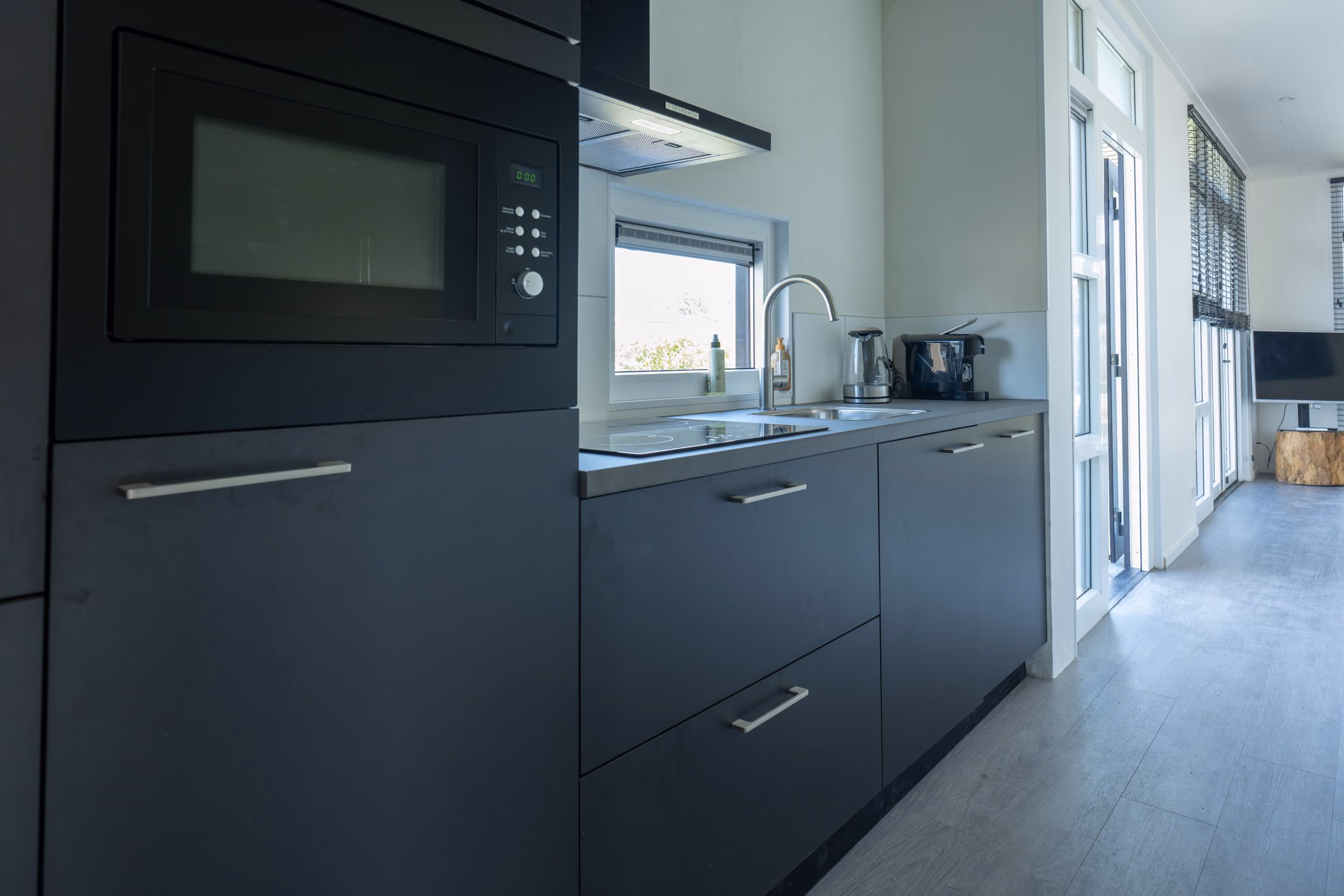 Modern kitchen with black cabinets, built-in microwave, stovetop, sink, coffee maker, and large windows.