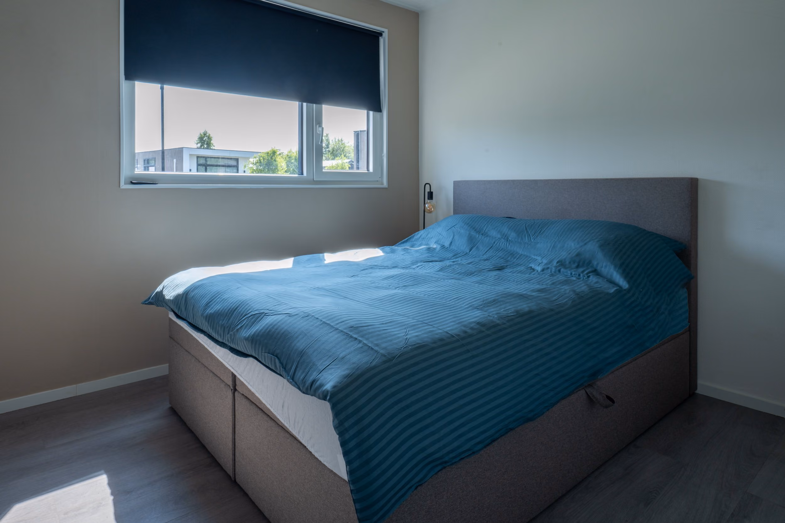 Minimalist bedroom with a gray bed frame and blue striped bedding under a window with a blue shade.