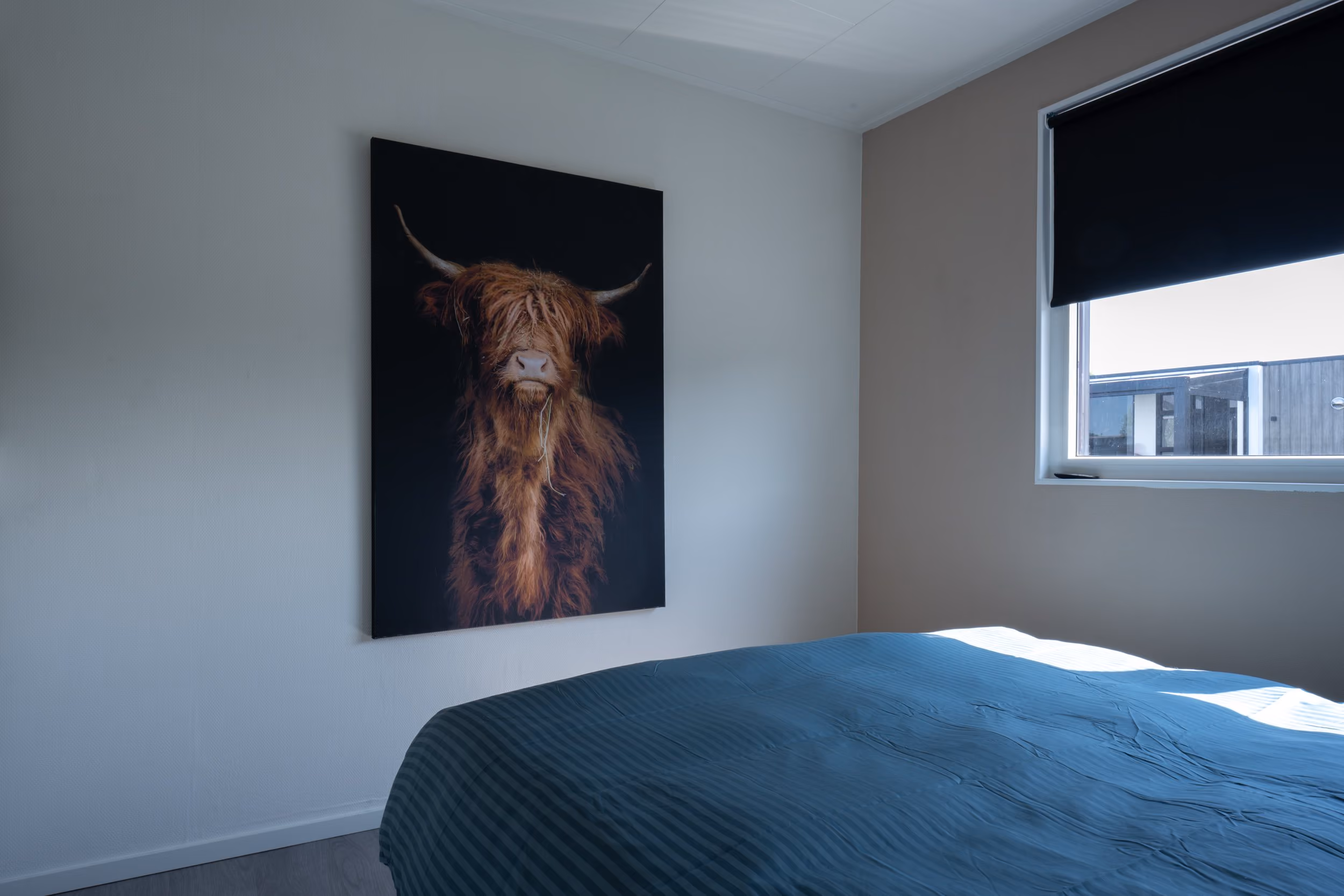 Bedroom with a bed covered in blue bedding and a wall painting of a brown highland cow with long hair.