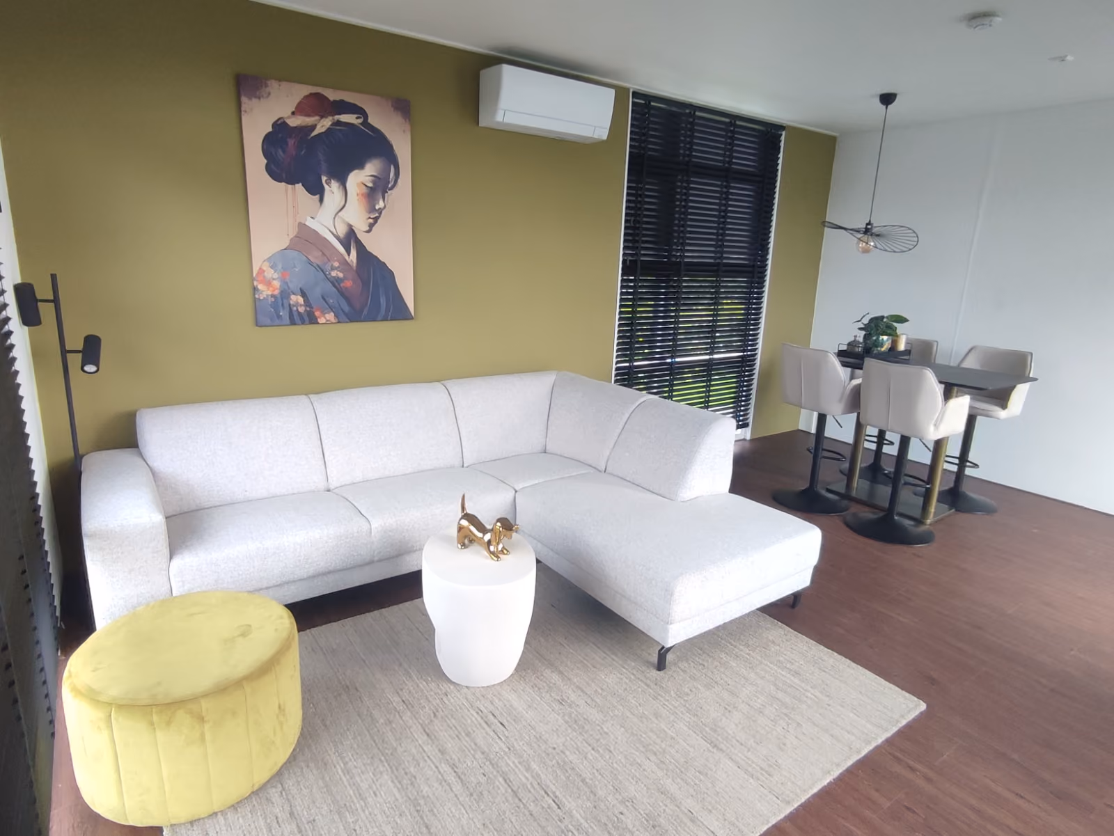 Modern living room with a white sectional sofa, yellow ottoman, small table, and dining area.