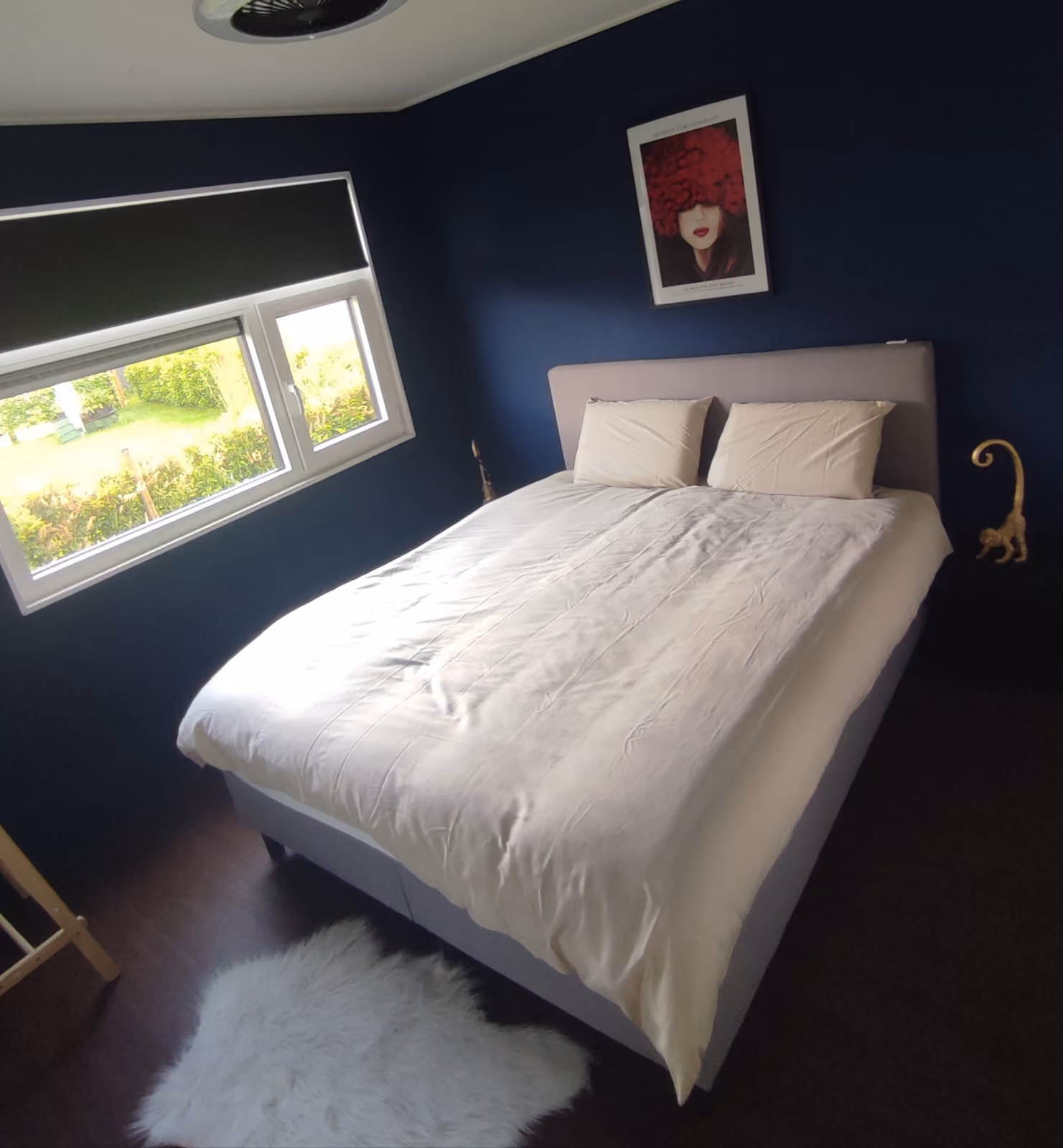 Bedroom with a neatly made bed, white bedding, blue walls, window, and framed red floral artwork.