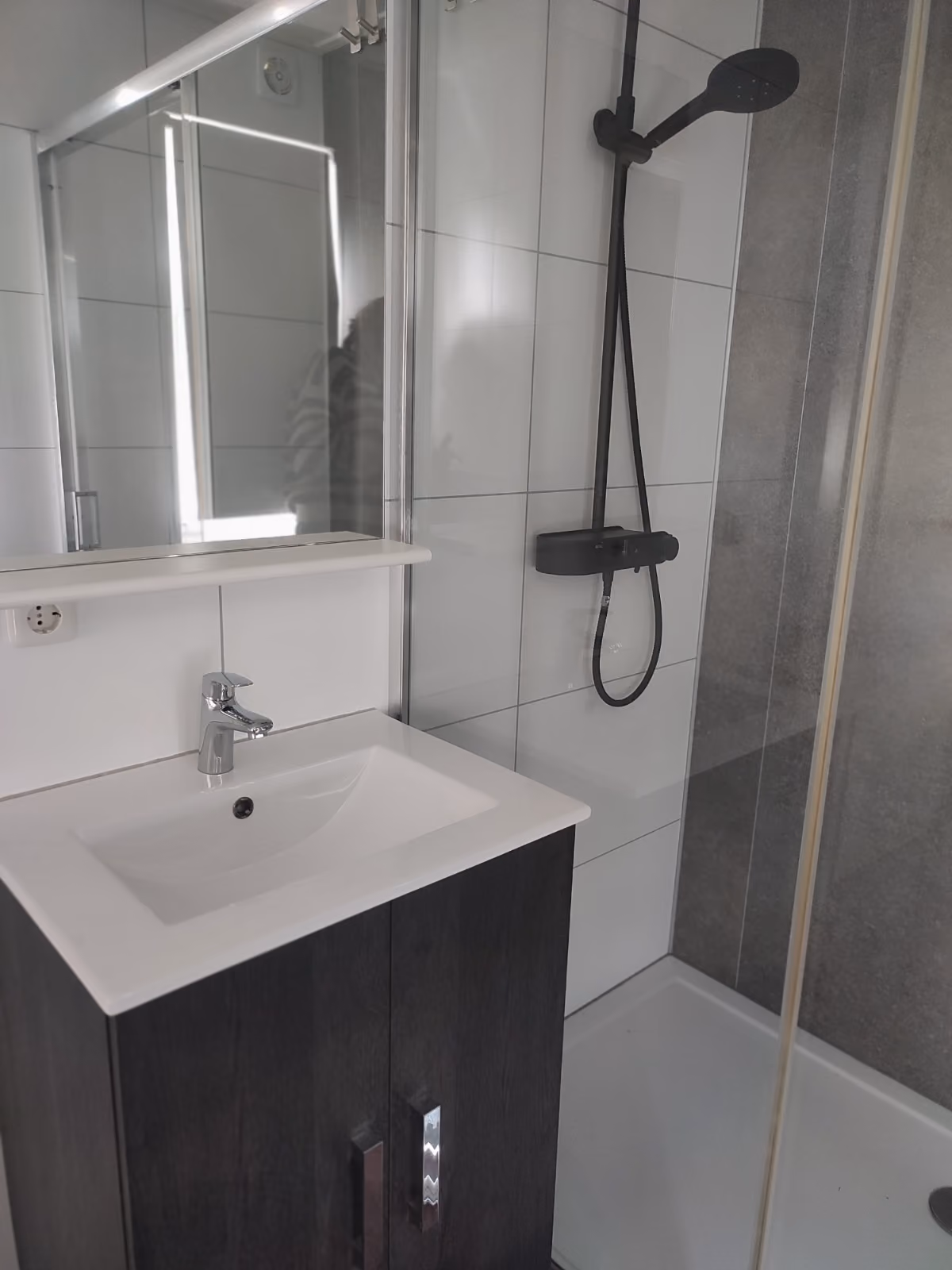 Modern bathroom sink with dark cabinet next to a glass shower with black showerhead and white tiles.