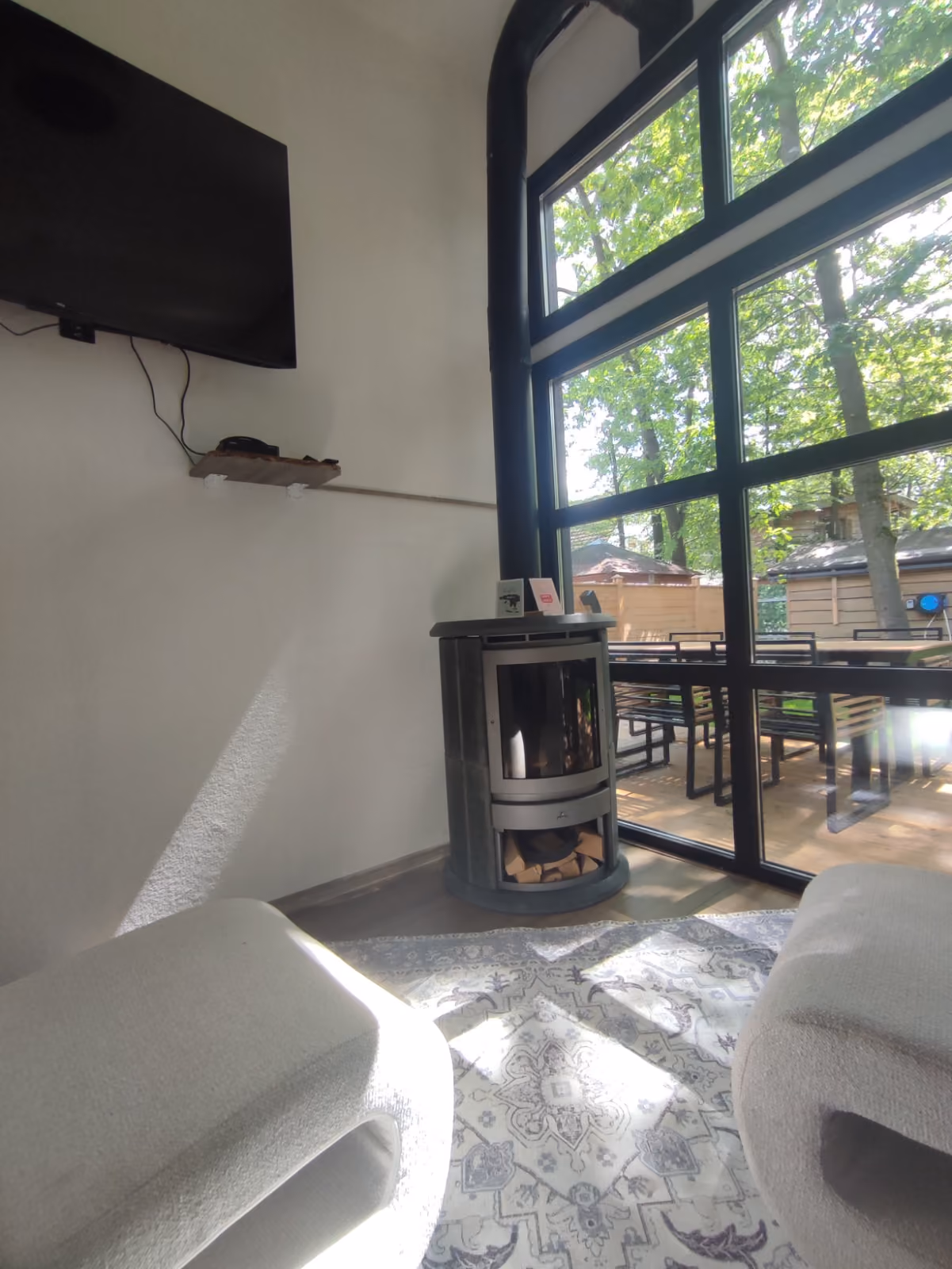 Cozy room corner with a modern stove, wall-mounted TV, large window, and patterned rug with soft seats.