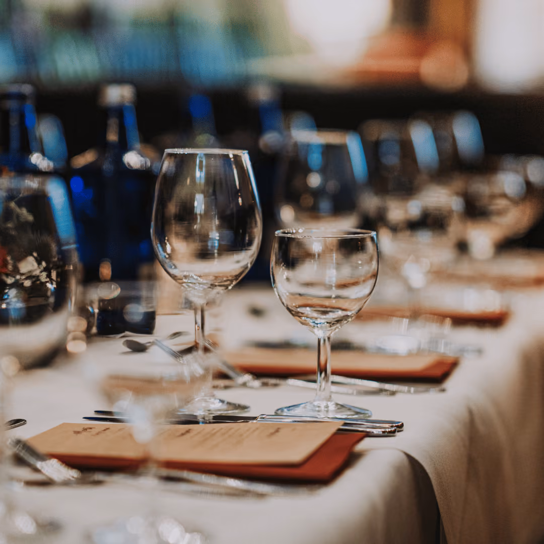 Close-up of empty wine glasses and menus on a white tablecloth at a formal dining table.