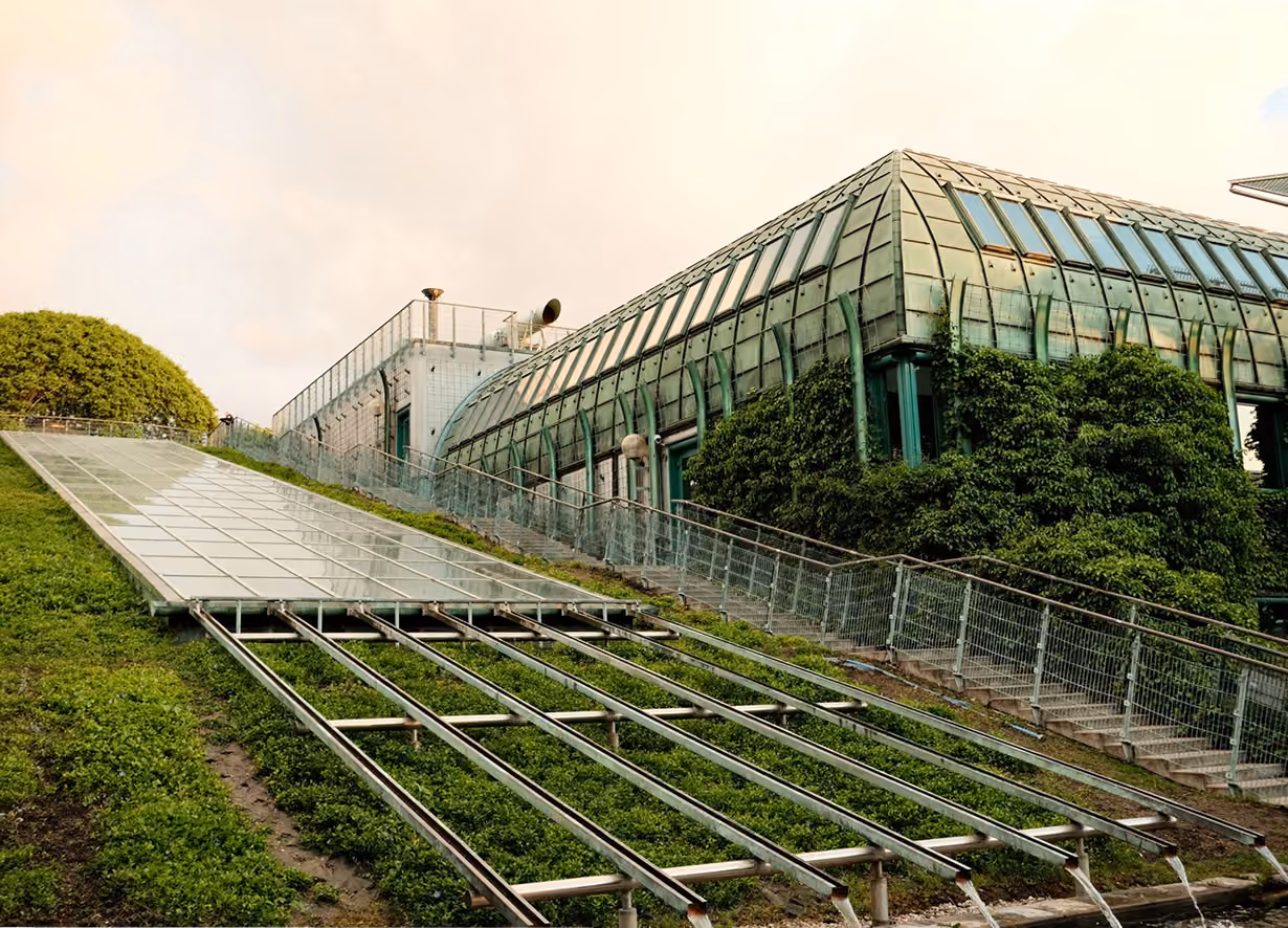 Gebouw met een glazen dak en groene begroeiing op een helling