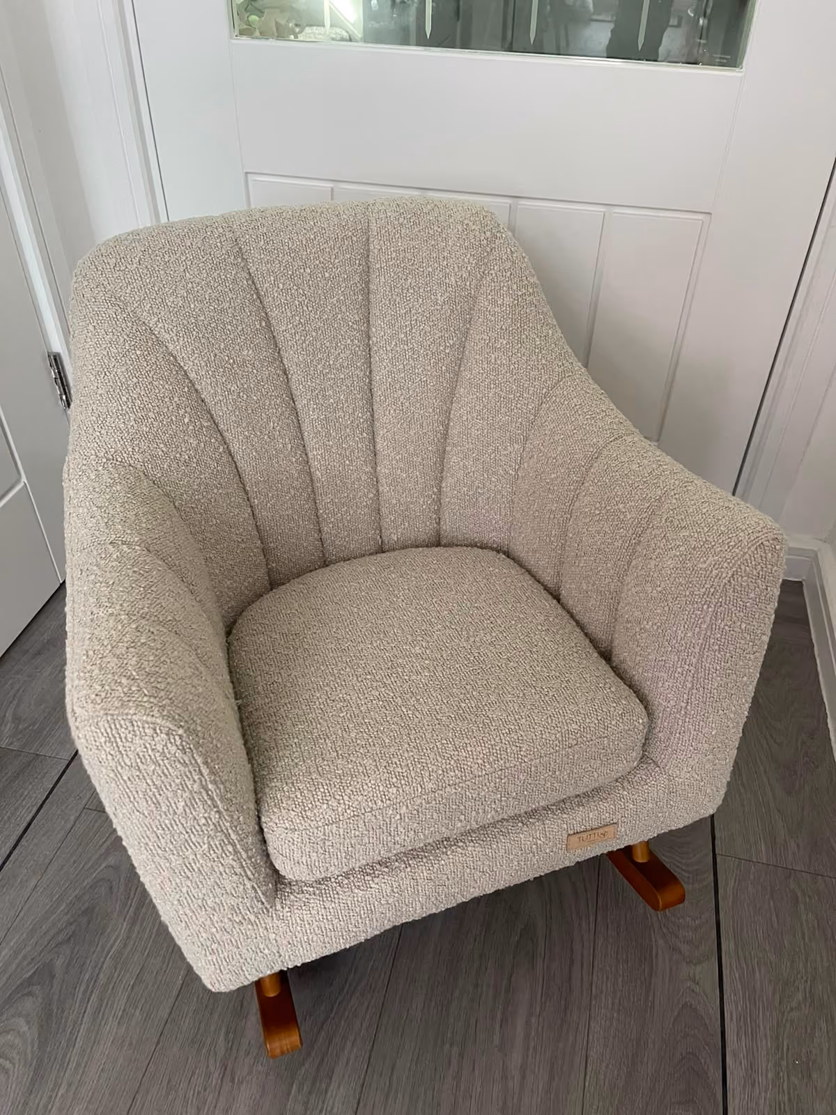 Beige textured fabric armchair with curved back and wooden rocker legs on gray floor.