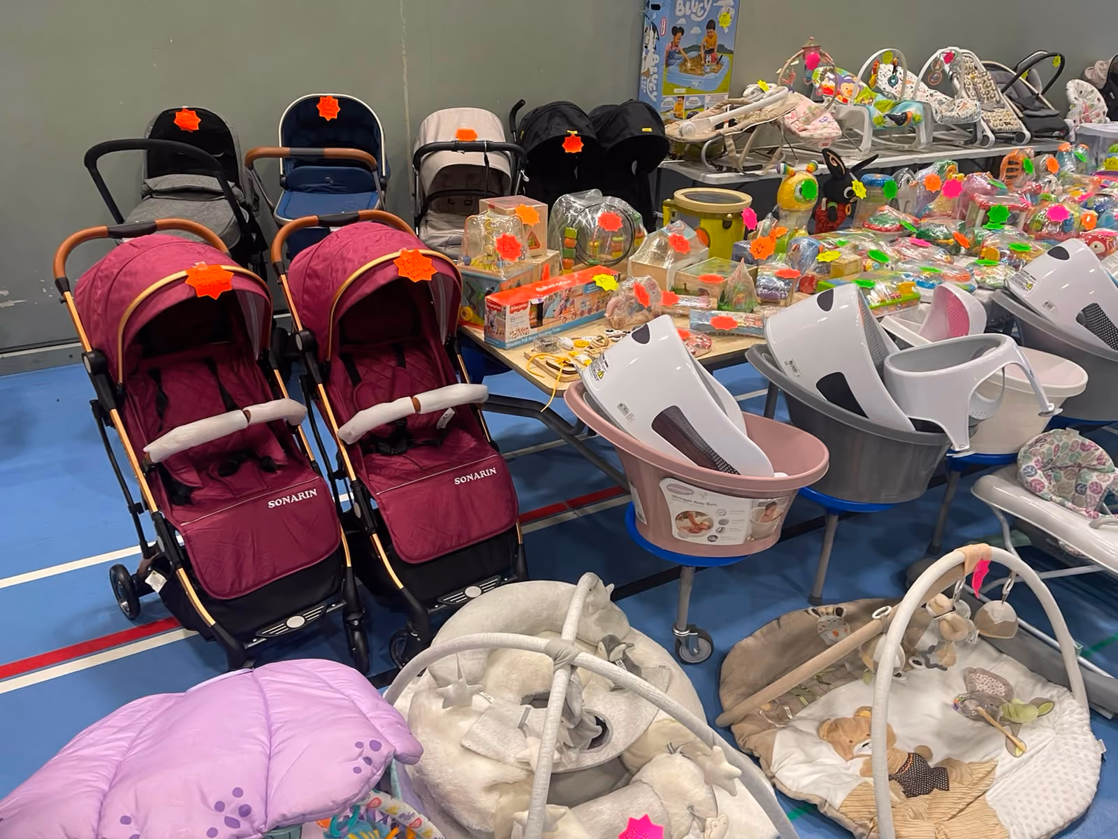 A display of baby products including strollers, toys, baby bathtubs, and play mats with price tags indoors.