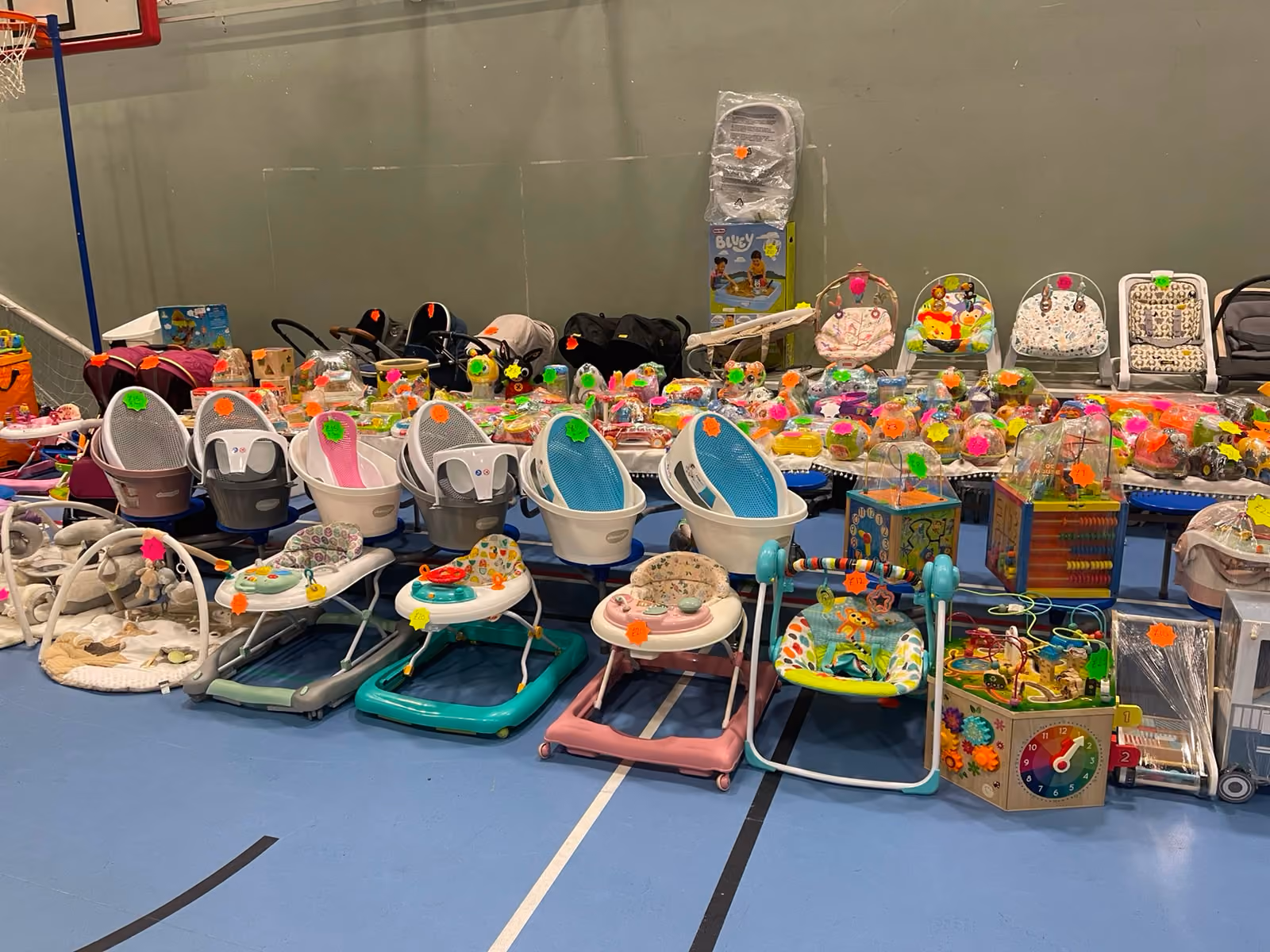 Various baby items including walkers, seats, toys, and bouncers arranged in rows on a gym floor.
