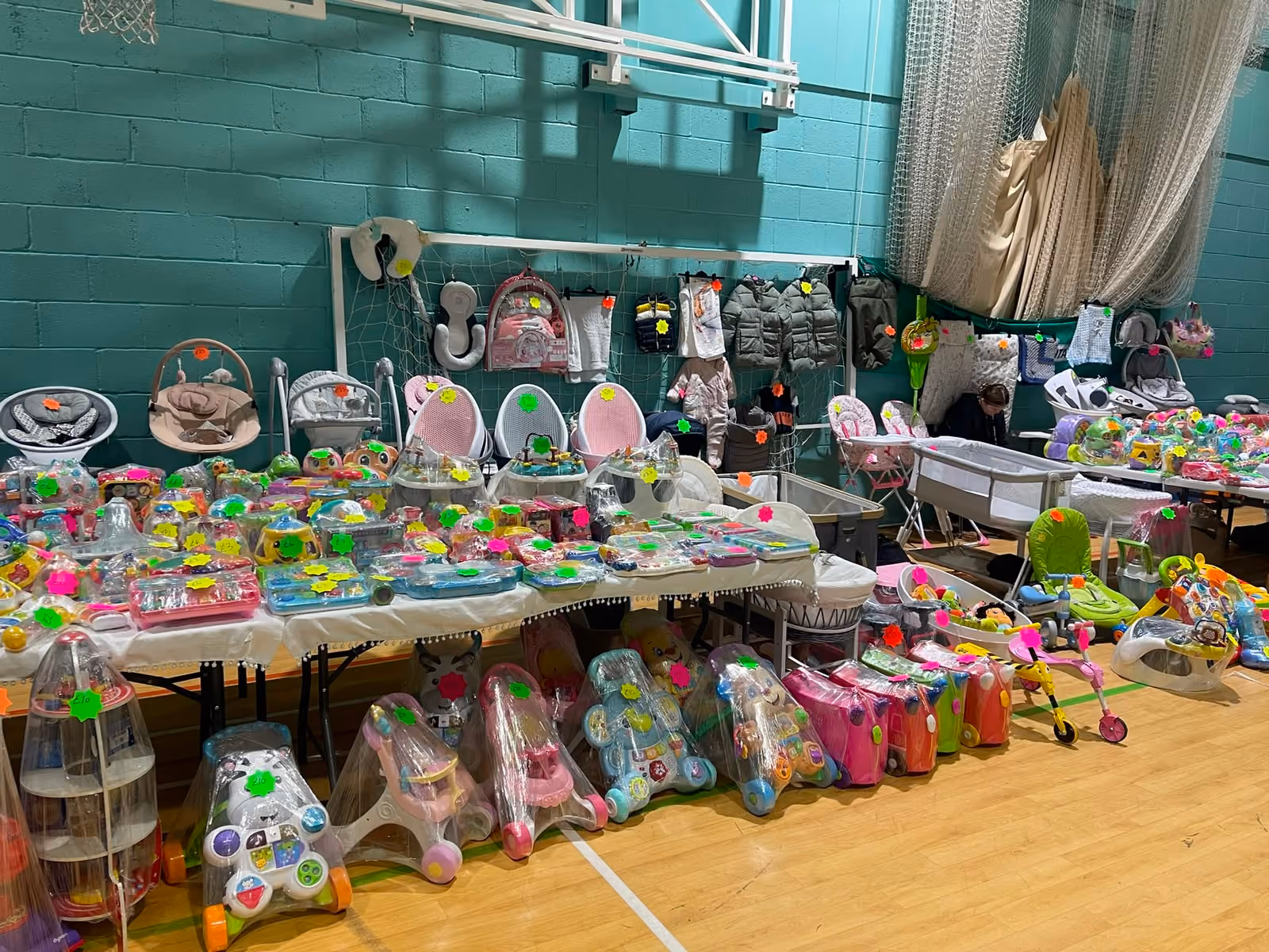 Indoor sale with tables displaying various baby items including toys, walkers, strollers, and clothes.