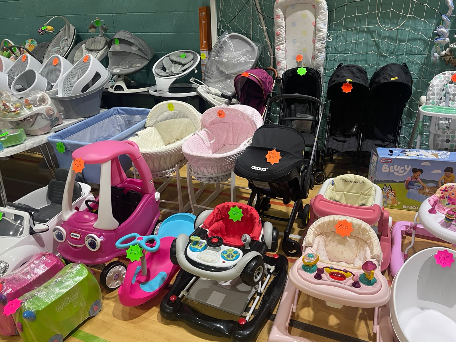 Various baby strollers, walkers, rockers, and toys with price tags in a store display.