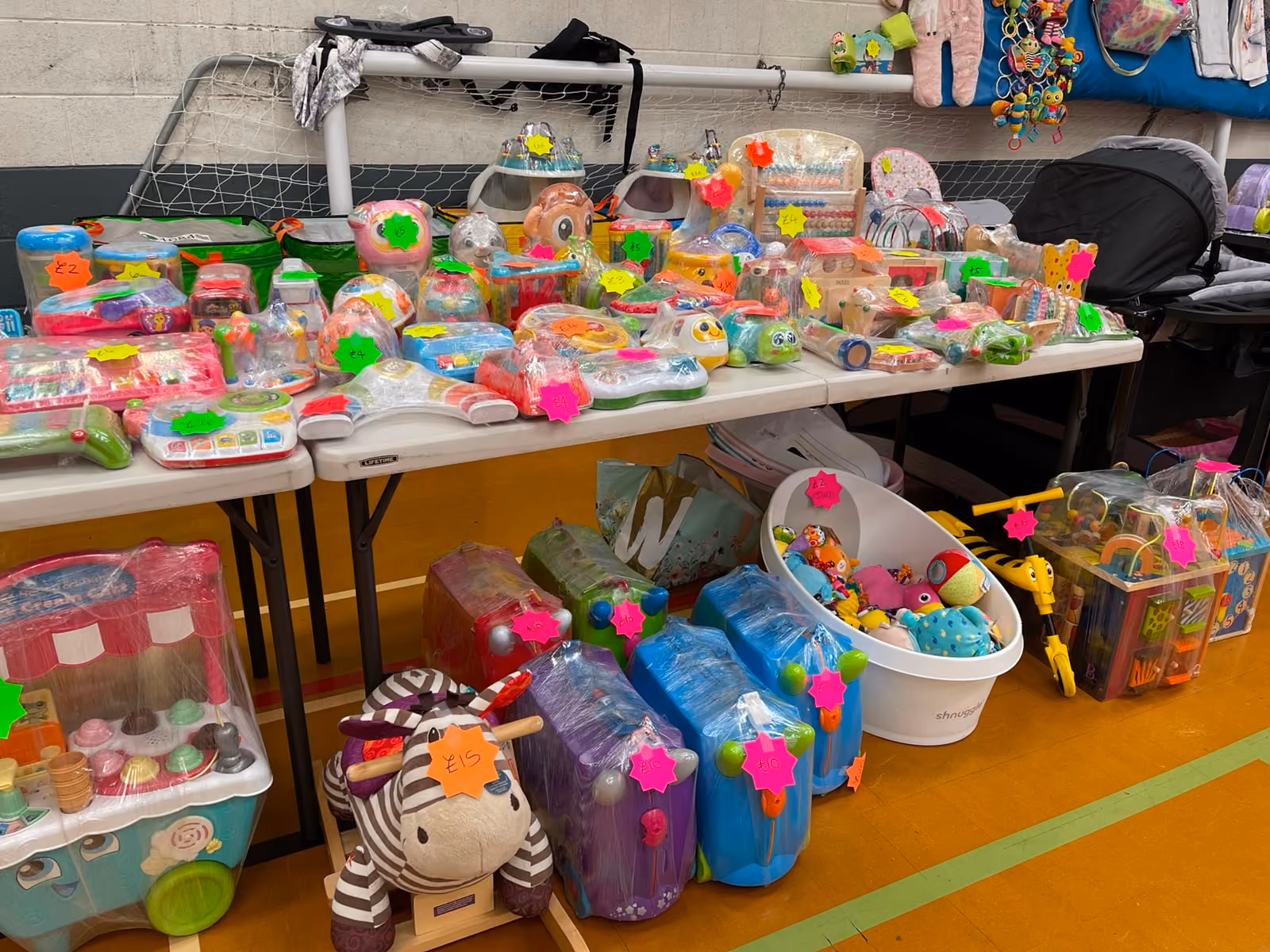 Tables displaying various children's toys with price tags in a gym or indoor space.