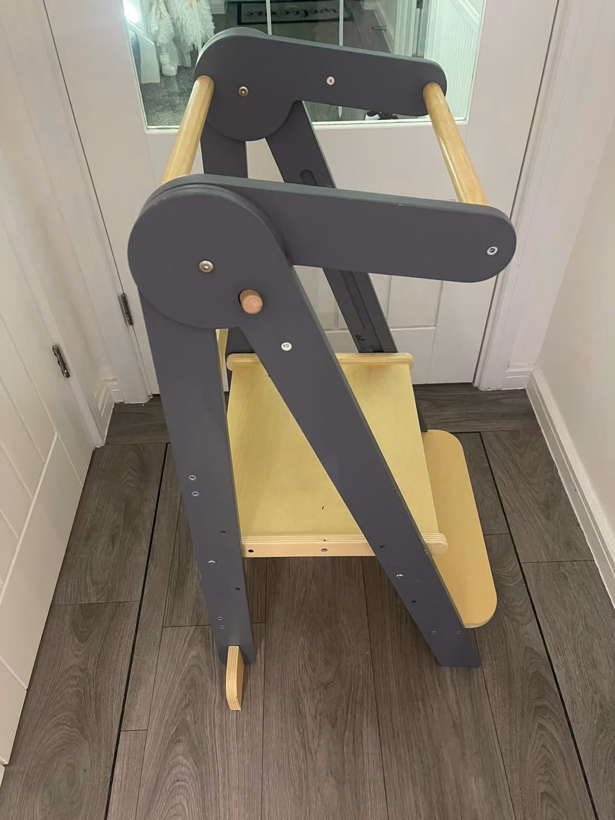 Folded wooden high chair with gray and natural wood finish on a dark floor near white doors.