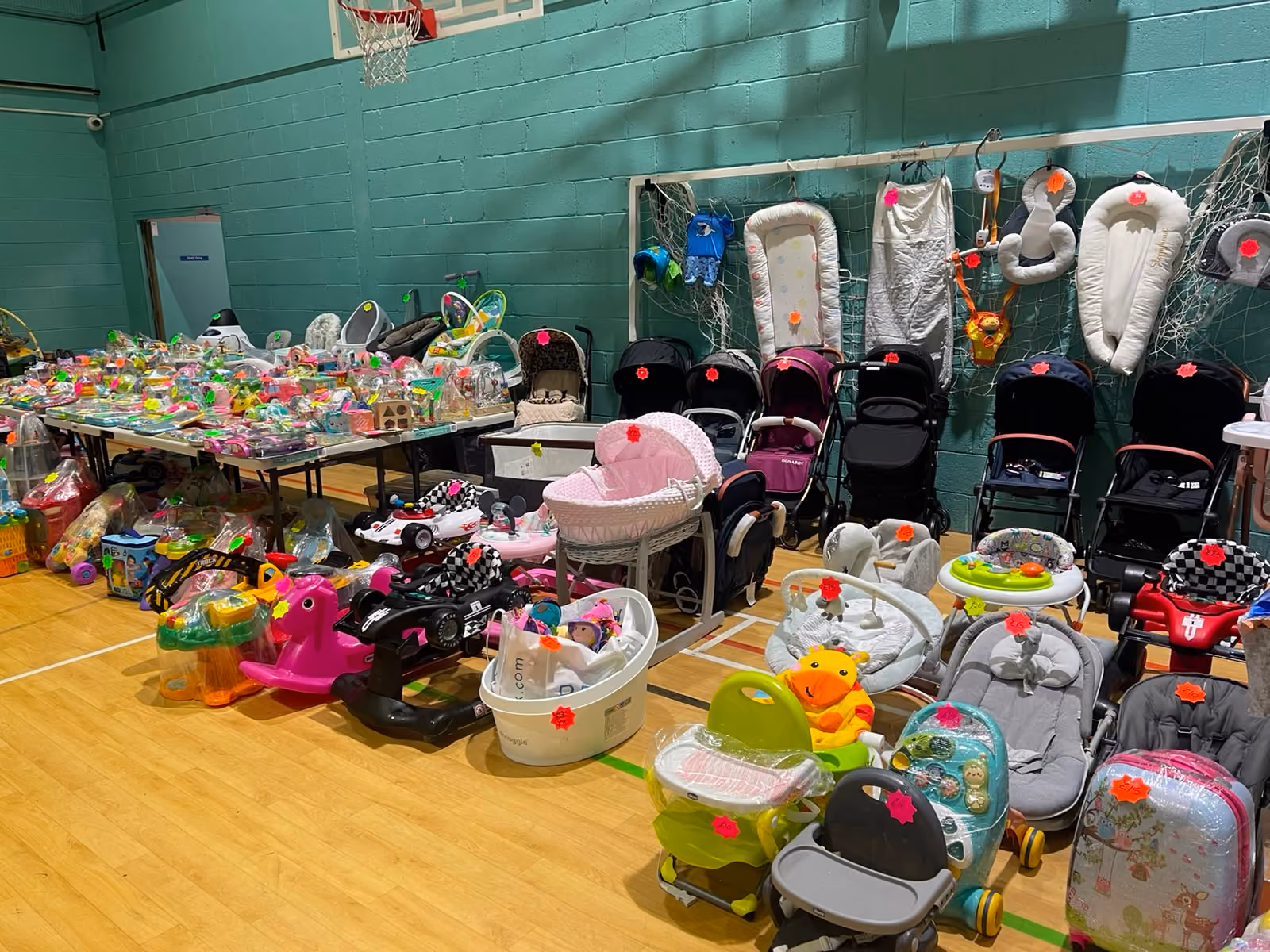 Various baby items including strollers, toys, and seats displayed for sale in a gymnasium.