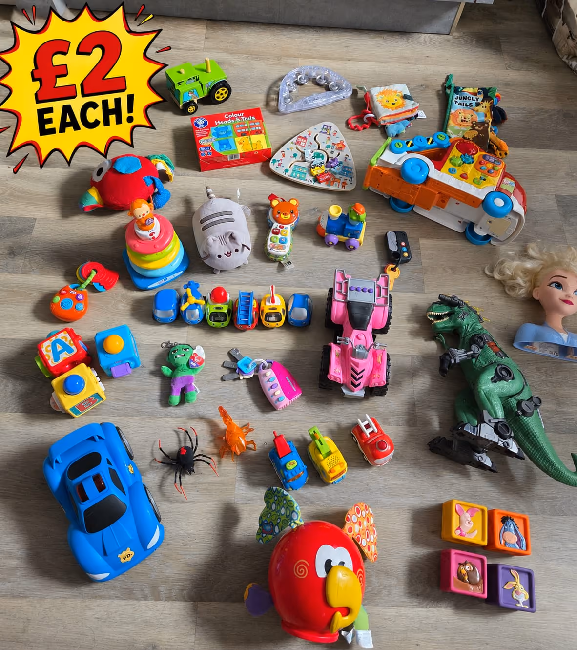 Various colorful children's toys laid out on a wooden floor with a £2 each sign.