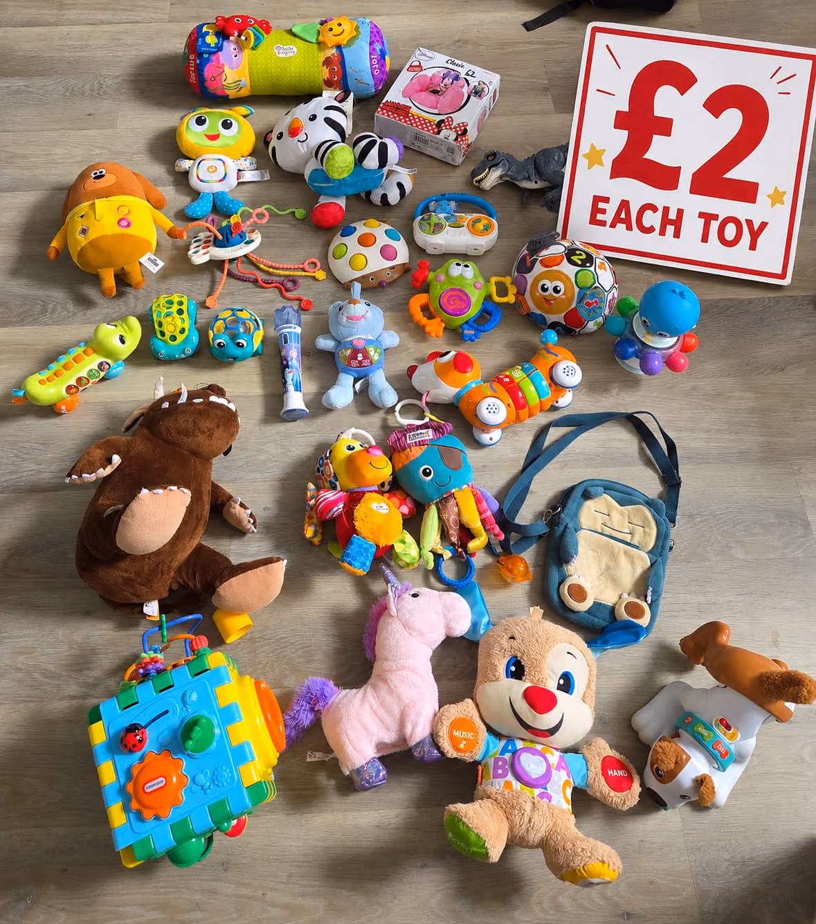 Variety of colorful children's toys displayed on wood floor with a sign reading £2 each toy.