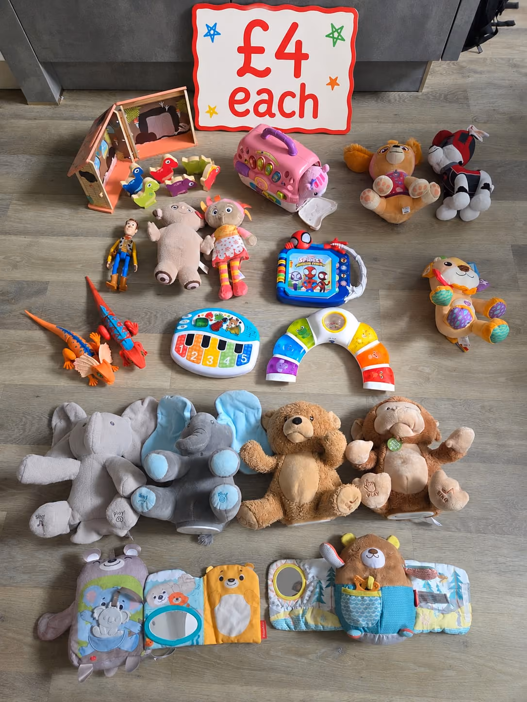 Various children’s toys including plush animals, dolls, and musical toys on a floor with a £4 each sign.