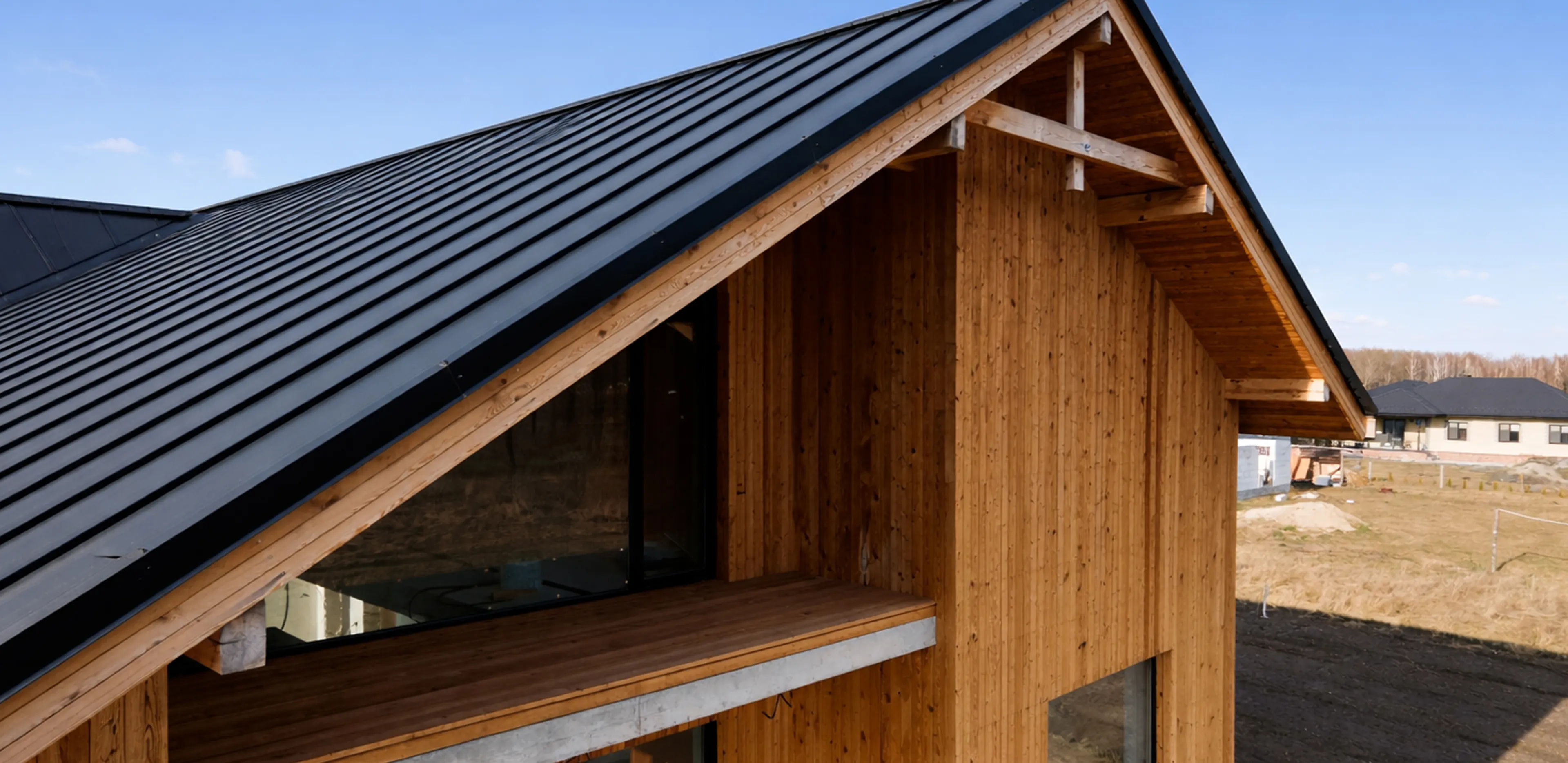 Modern wooden house with a black metal sloped roof and large windows during daytime.
