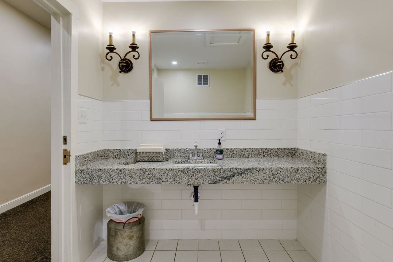 Restroom with a granite trough counter and sink, white subway tile wainscot, a framed mirror and wall sconces
