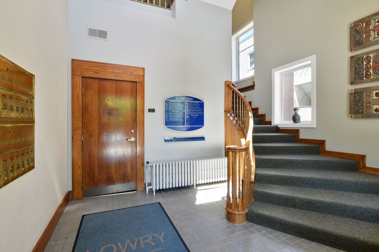 Entry vestibule with a wood door, a bank of brass mailboxes, a cast-iron radiator and the staircase rising at right