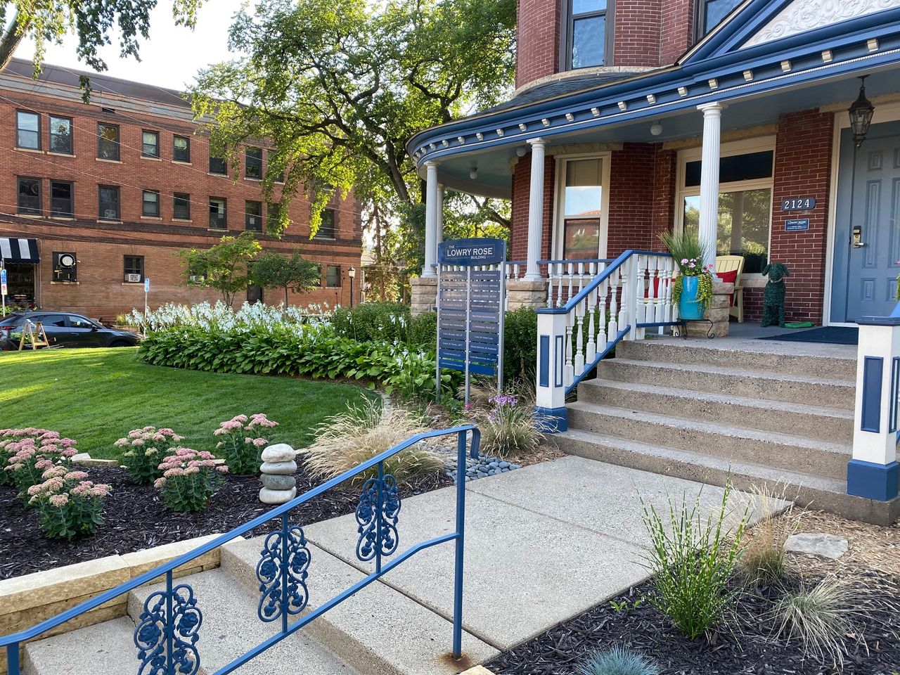 Front entry steps seen from the sidewalk with blue iron railings and autumn planting