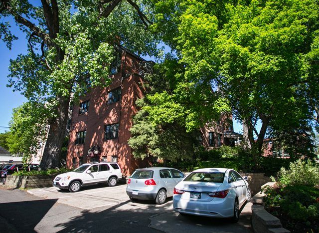 Brown brick building behind a surface parking lot with parked cars