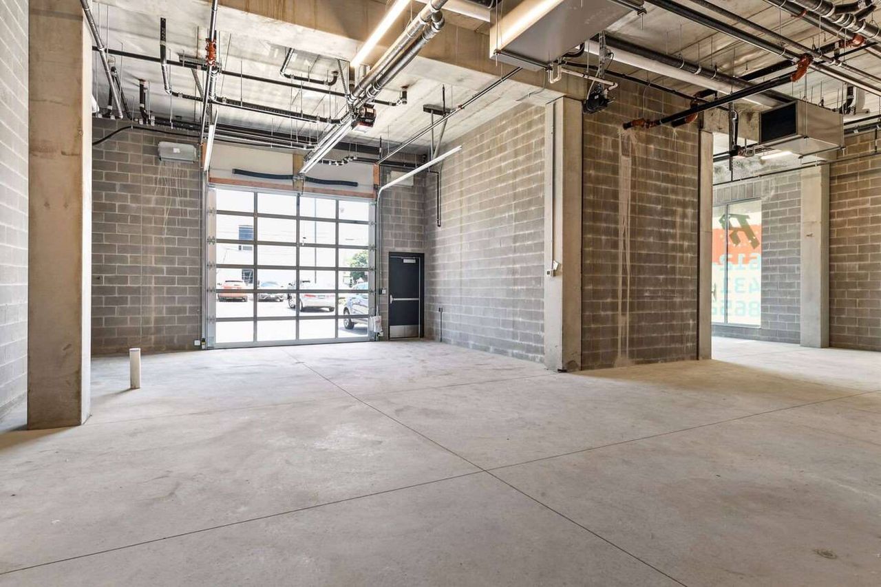 Unfinished ground-floor commercial space with concrete block walls, a glazed overhead door and a bare concrete floor