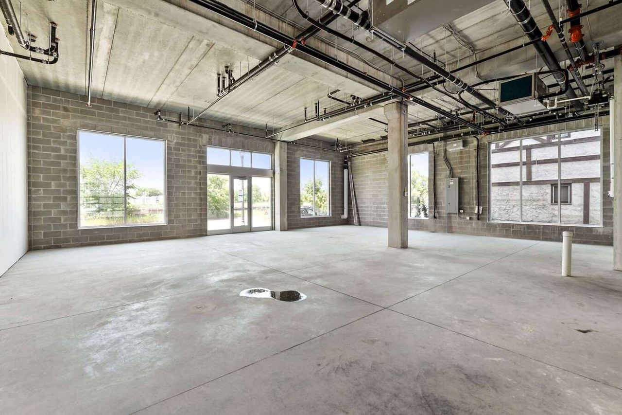 Wide unfinished commercial space with two window walls, a glazed double door and exposed concrete columns and beams