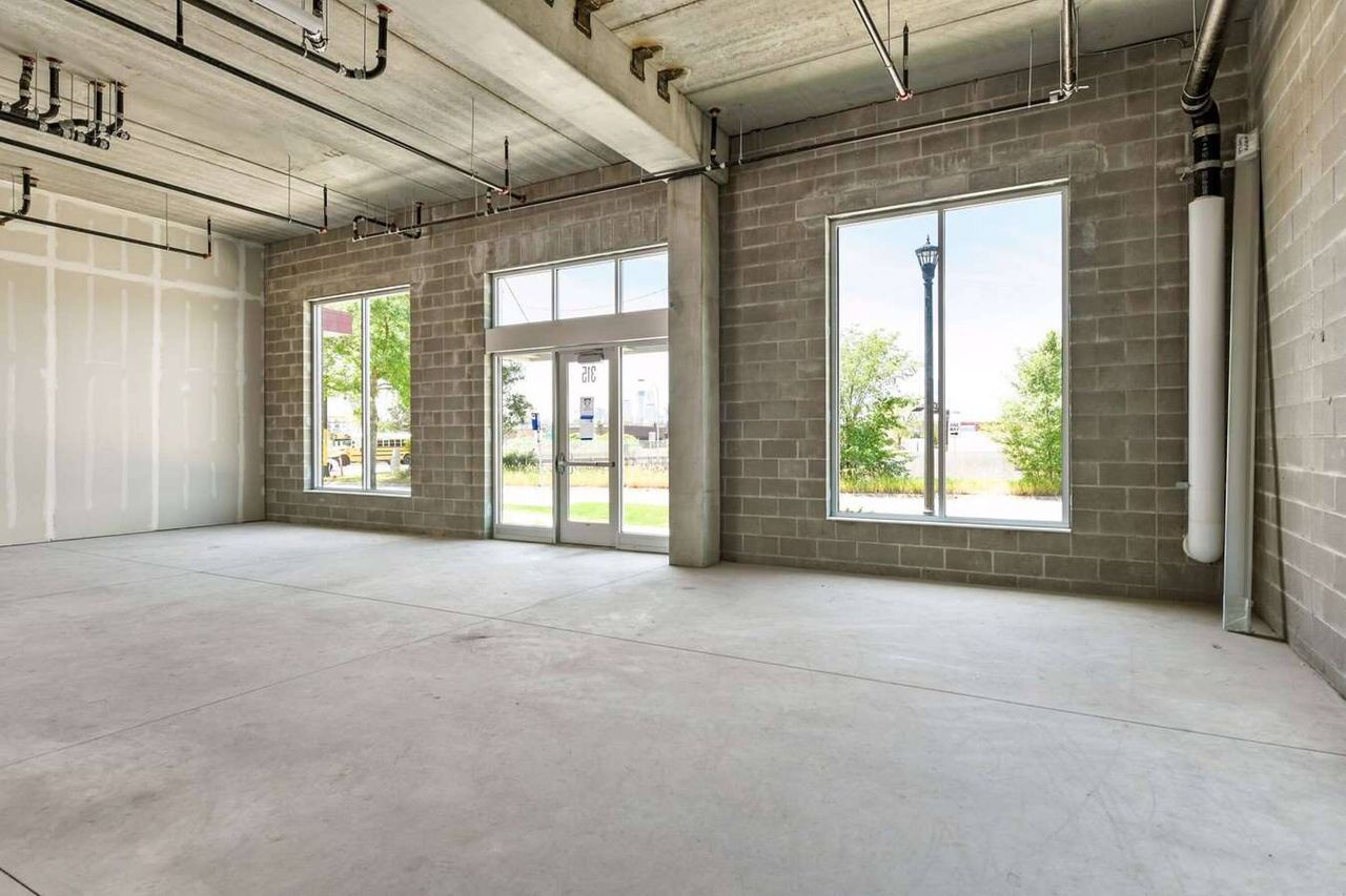 Unfinished corner commercial space with concrete block walls, a glazed double door and two large windows looking onto a lawn and street