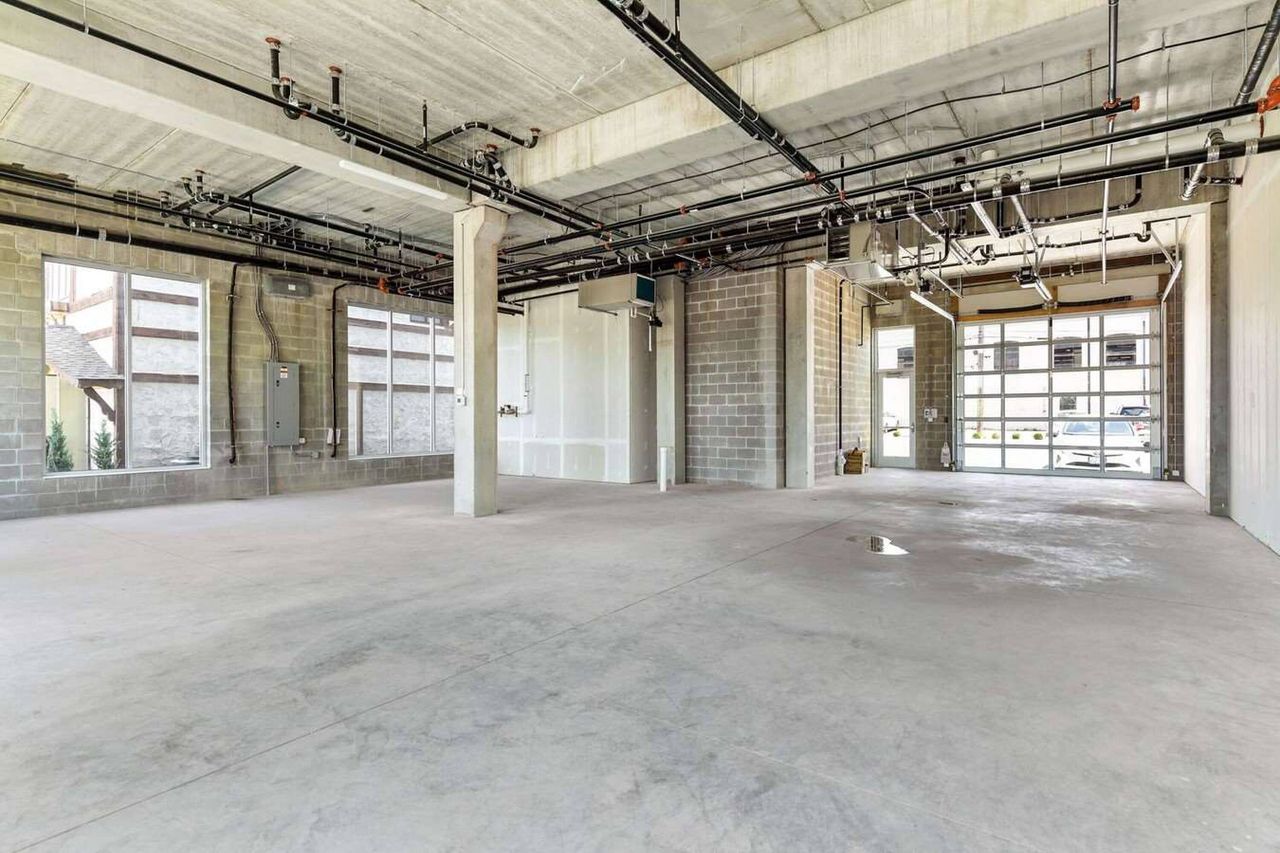 Deep unfinished commercial space with a central round column, exposed sprinkler piping and a glazed overhead door at the far end