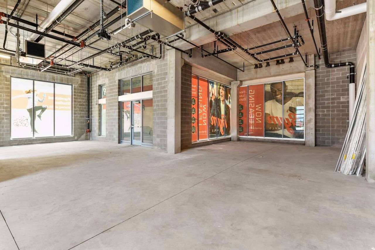 Unfinished commercial space with storefront glazing covered by large printed graphics, exposed ceiling services and a wood-toned soffit