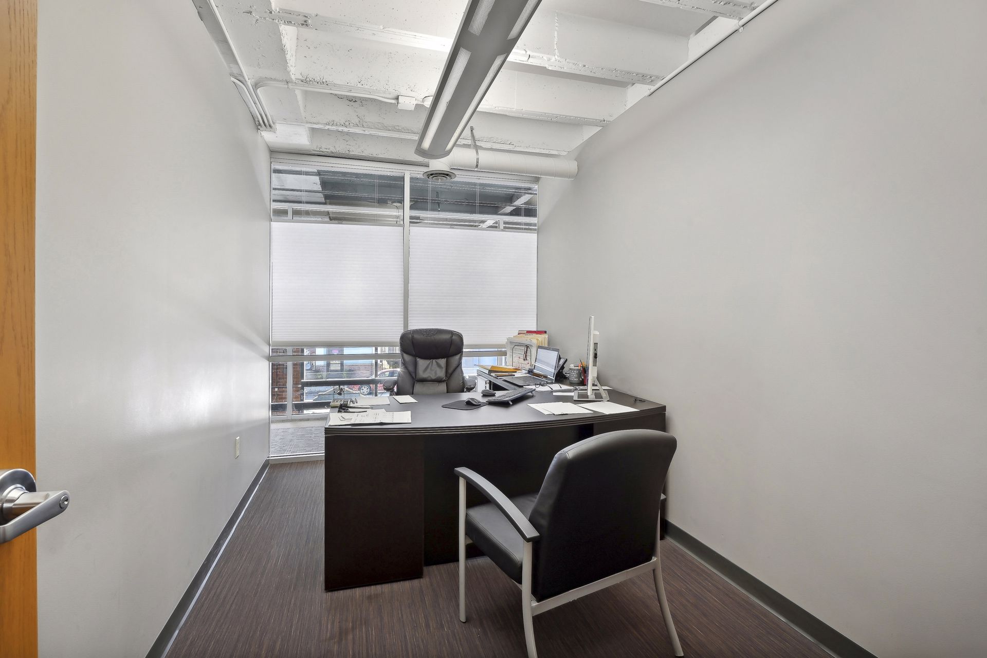Small private office with a dark wood desk and a roller-shaded window