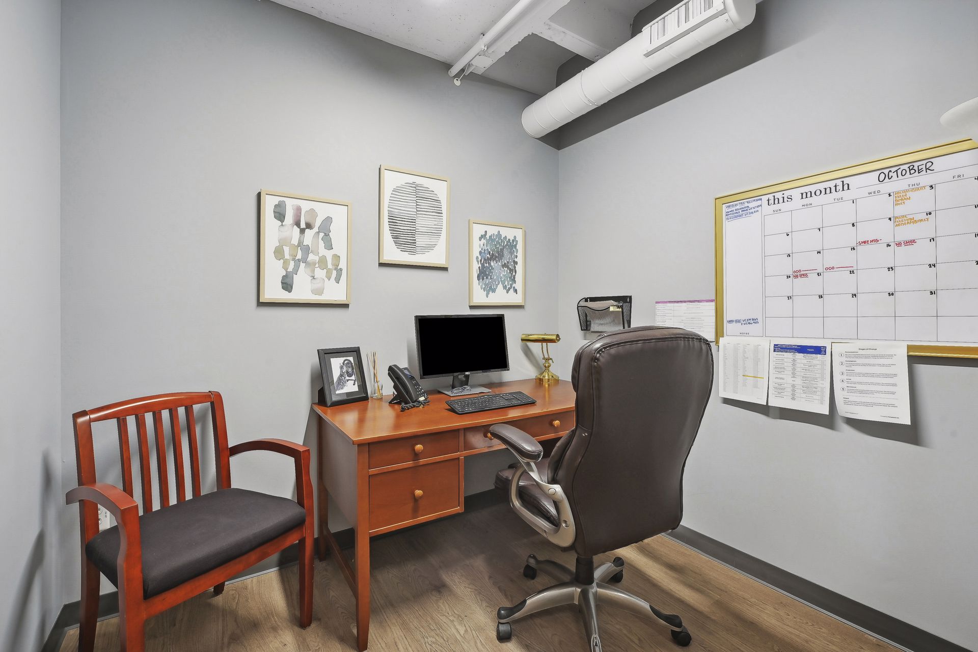 Office with a wood desk, framed artwork and a wall calendar