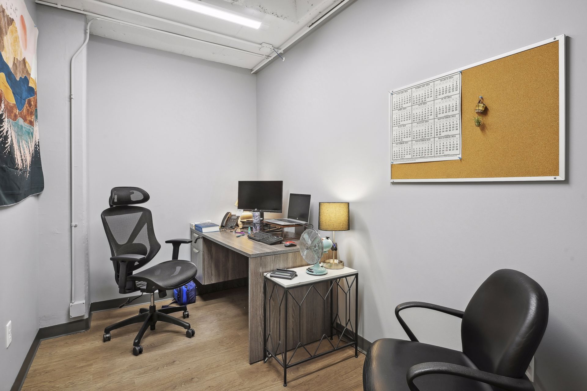 Small office with grey walls, a desk and a corkboard calendar