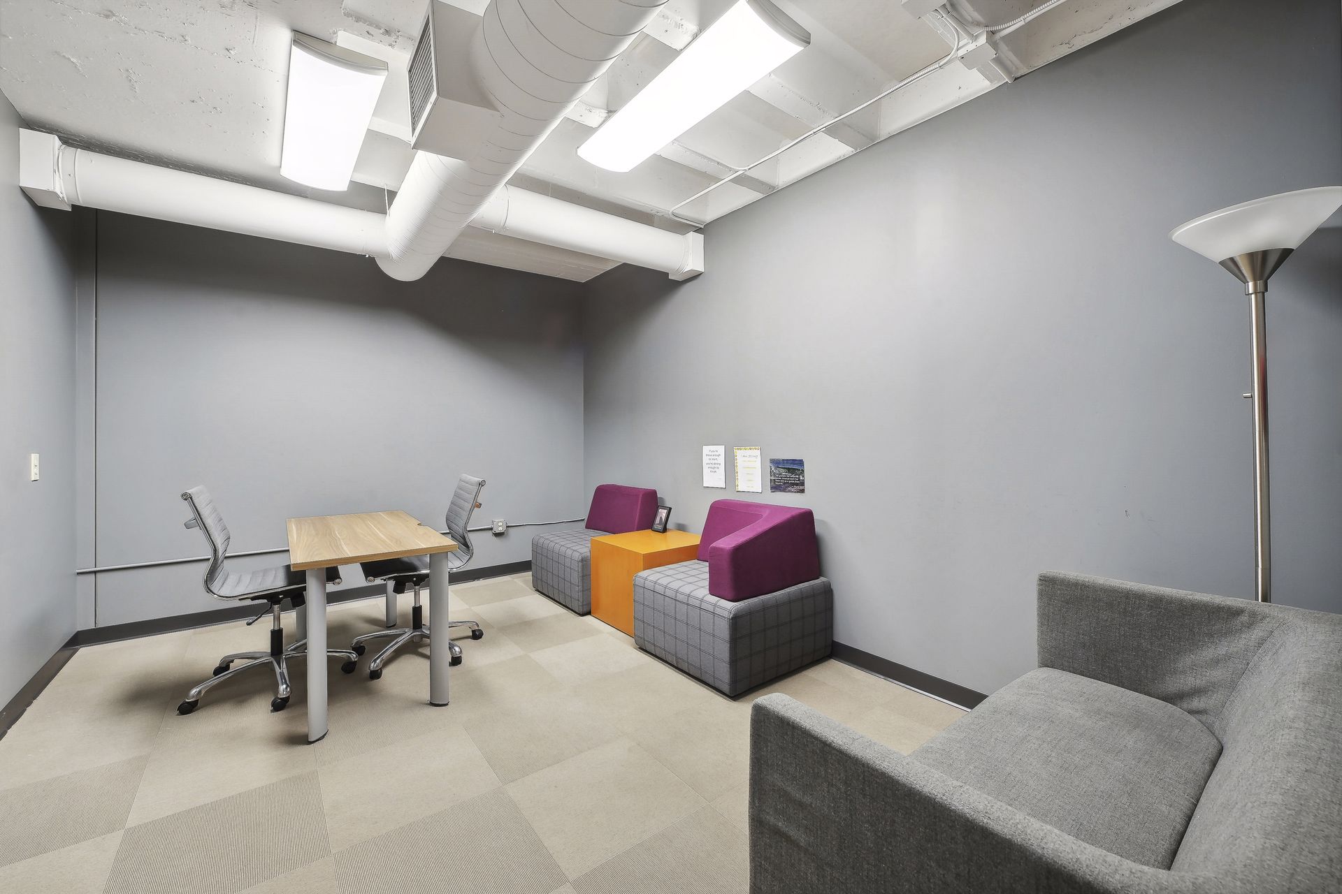 Small team room with grey walls, a meeting table and brightly upholstered lounge seating
