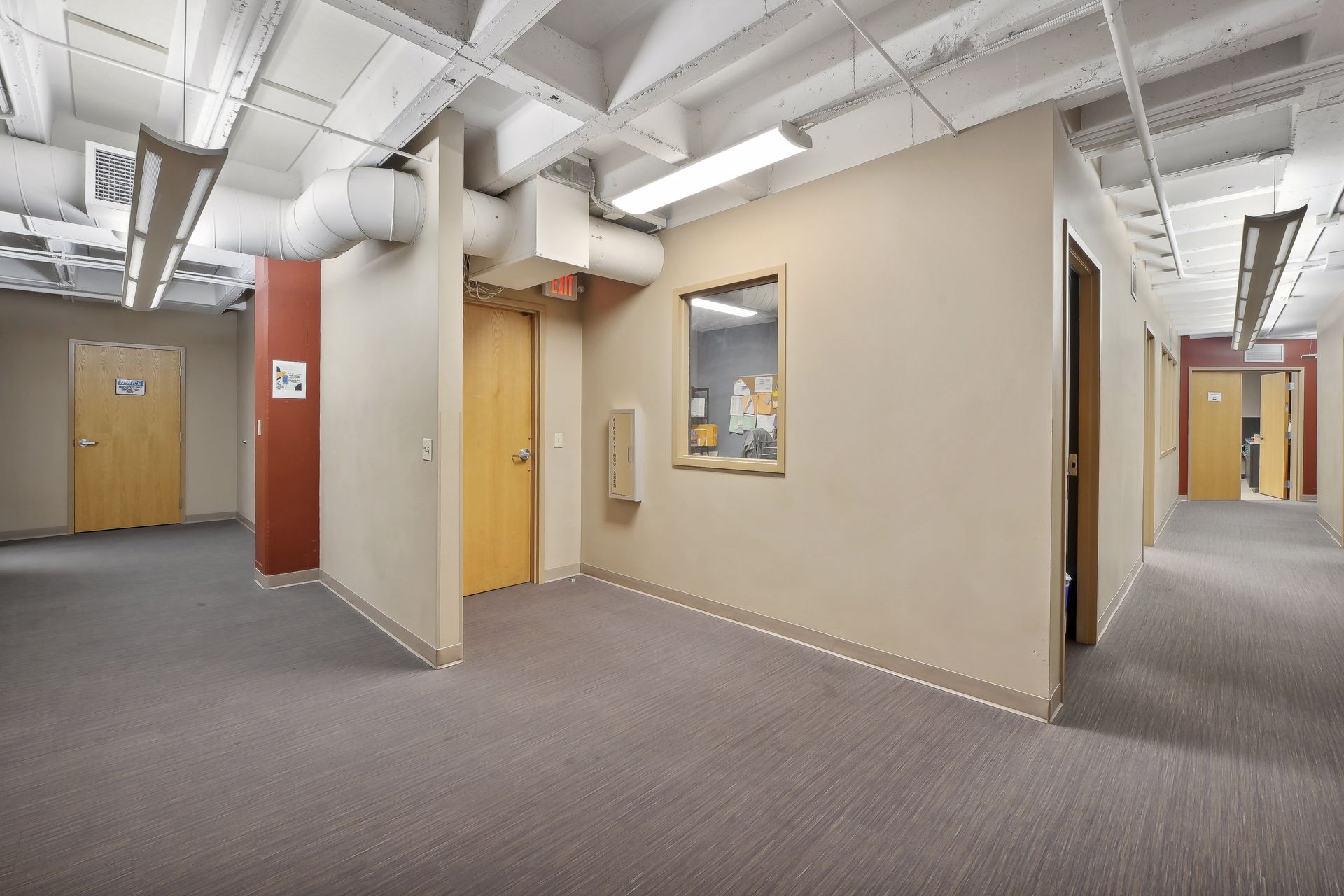 Corridor with tan and rust painted walls, wood doors and exposed spiral ductwork overhead