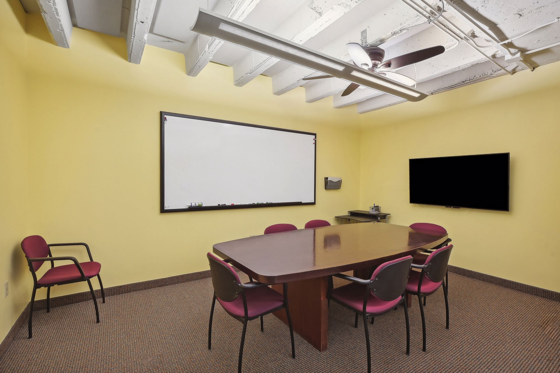 Conference room with yellow walls, a whiteboard, a wall-mounted display and upholstered chairs