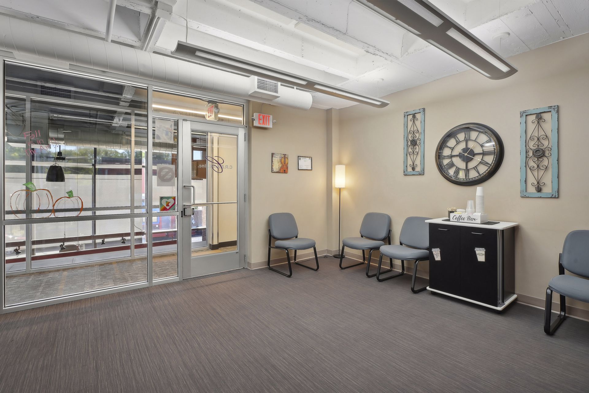 Waiting area with guest chairs, a coffee bar and a wall clock beside a glazed entrance
