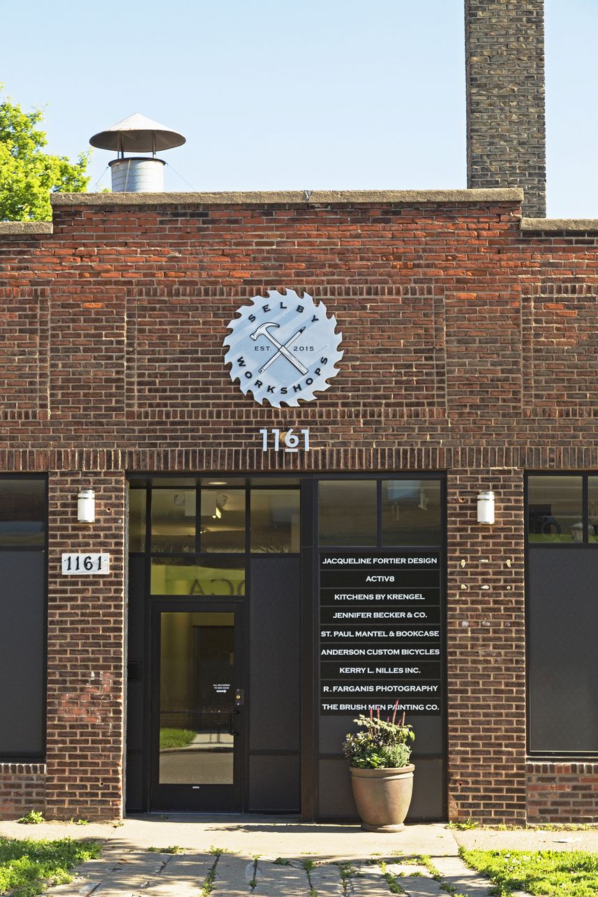 Close view of the brick entrance bay with a circular saw-blade sign reading Selby Workshops, address numerals and a glass door