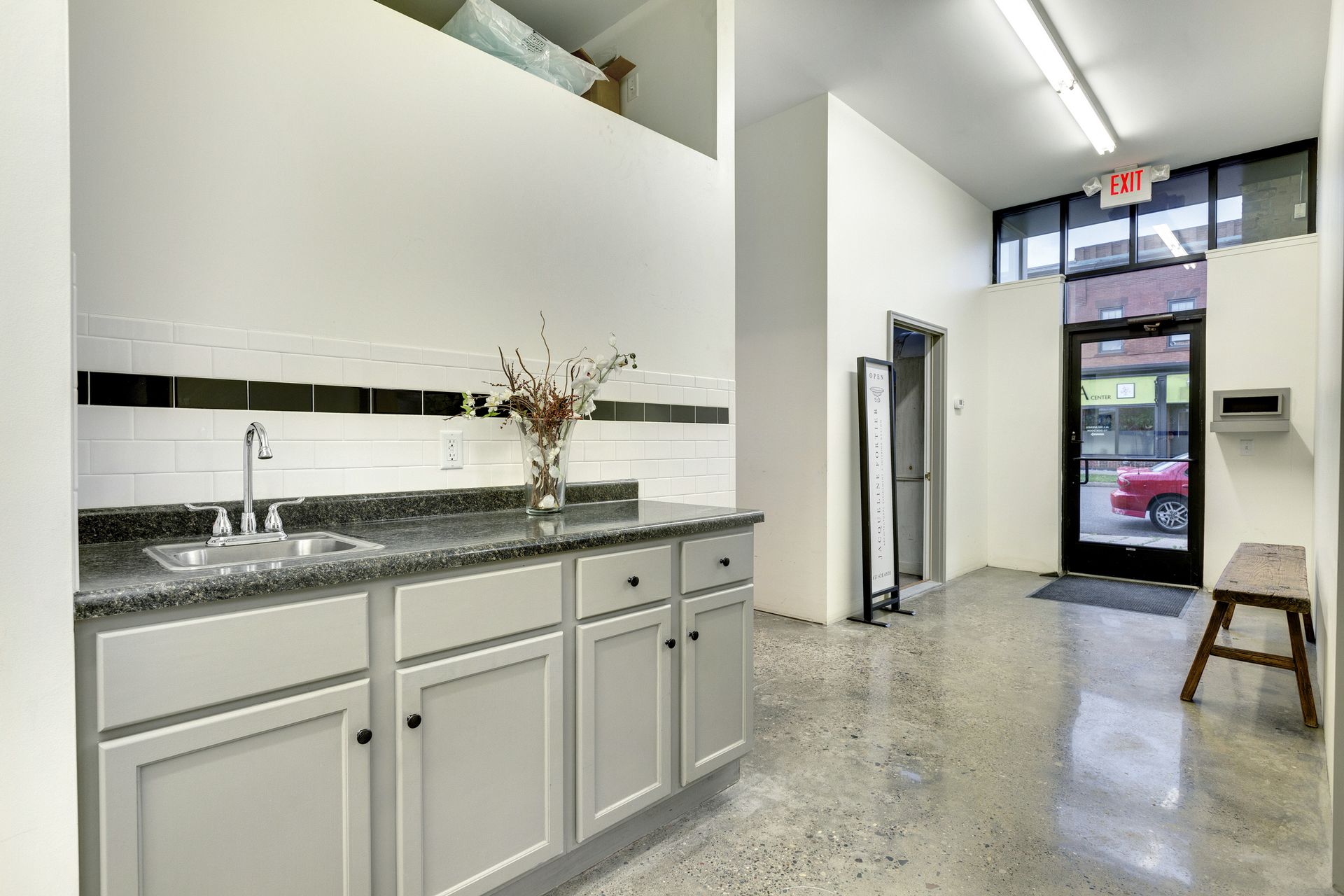 Kitchenette with grey shaker cabinets, a dark granite counter, white subway tile and a polished concrete floor