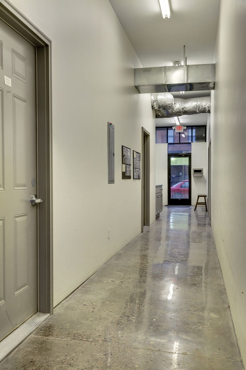 Corridor with panelled doors, a metal electrical panel, framed notices on the wall and a glazed entrance door at the end