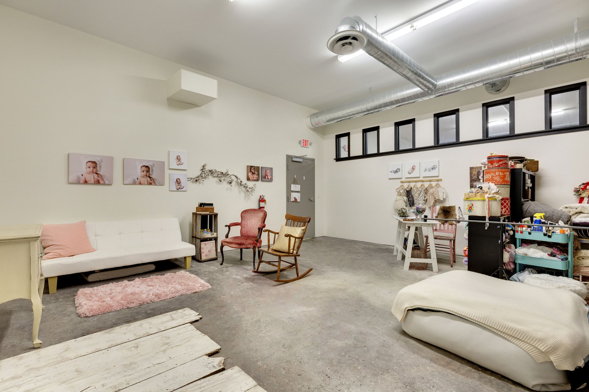 Studio with canvas portrait prints on the wall, a white sofa, a pink rug, a rocking chair and a row of clerestory windows