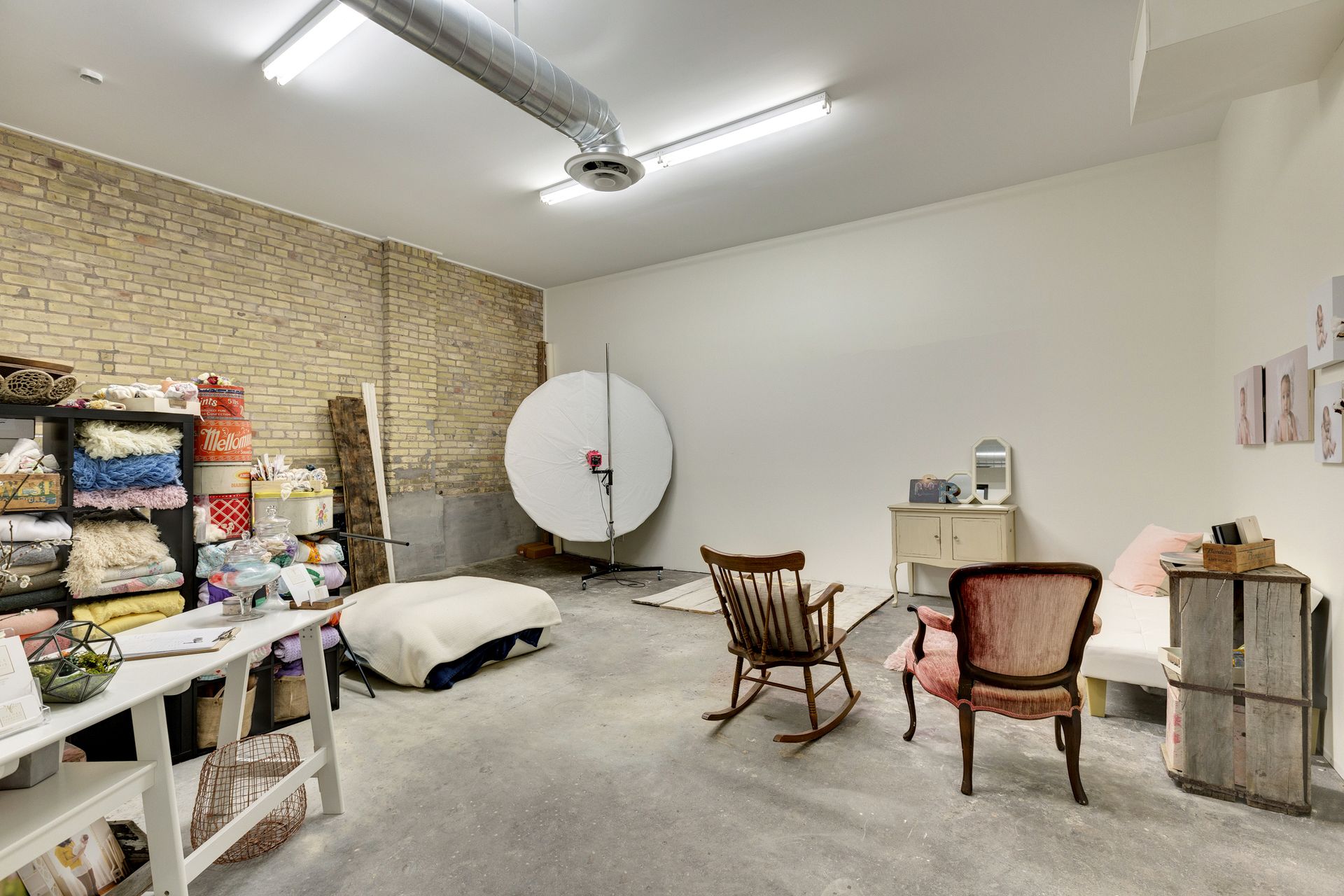 Studio room with a large white circular reflector, a wooden rocking chair, an upholstered armchair and shelving stacked with fabric