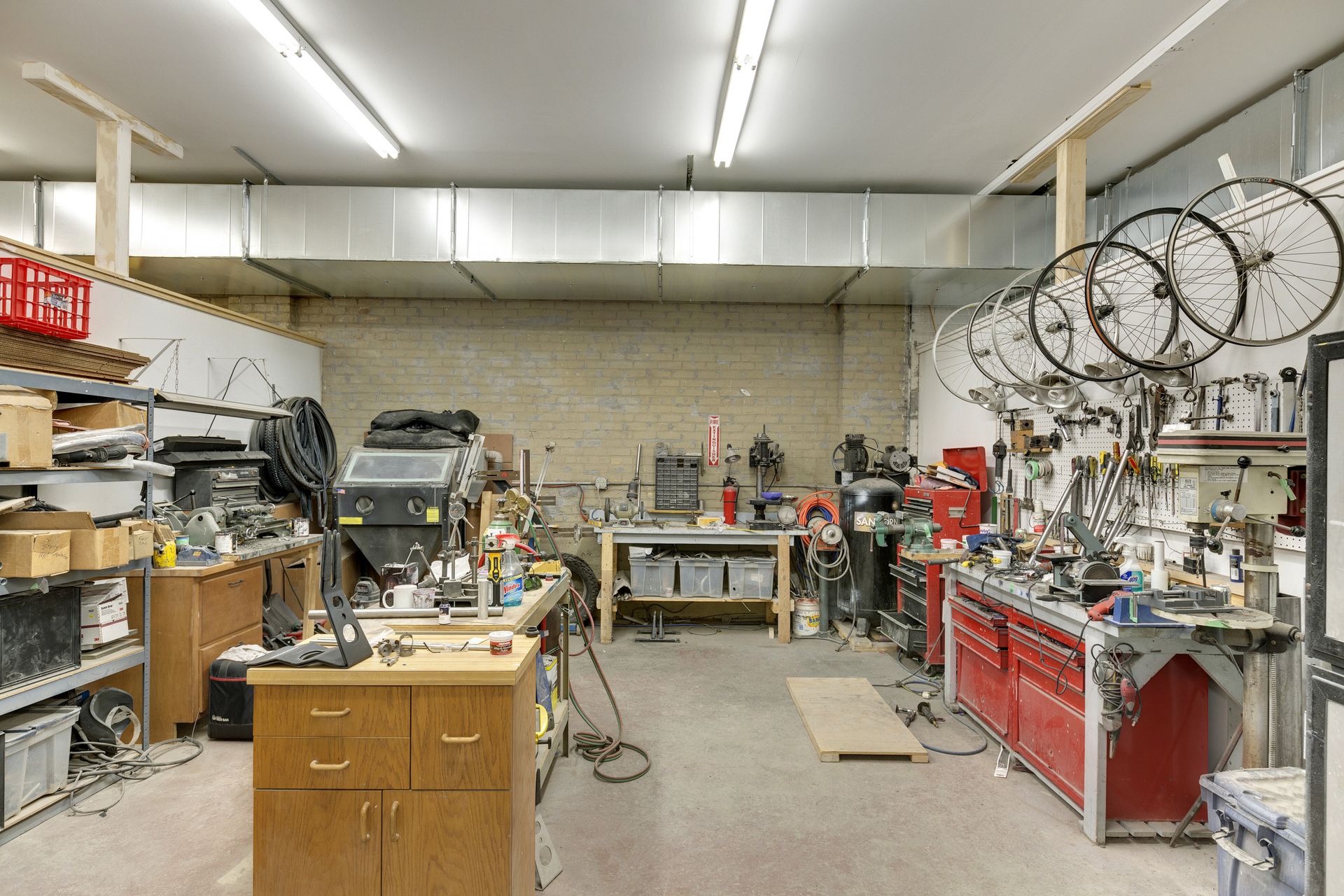 Bicycle workshop with wheels hung on the wall, a red rolling tool chest, workbenches and overhead strip lighting