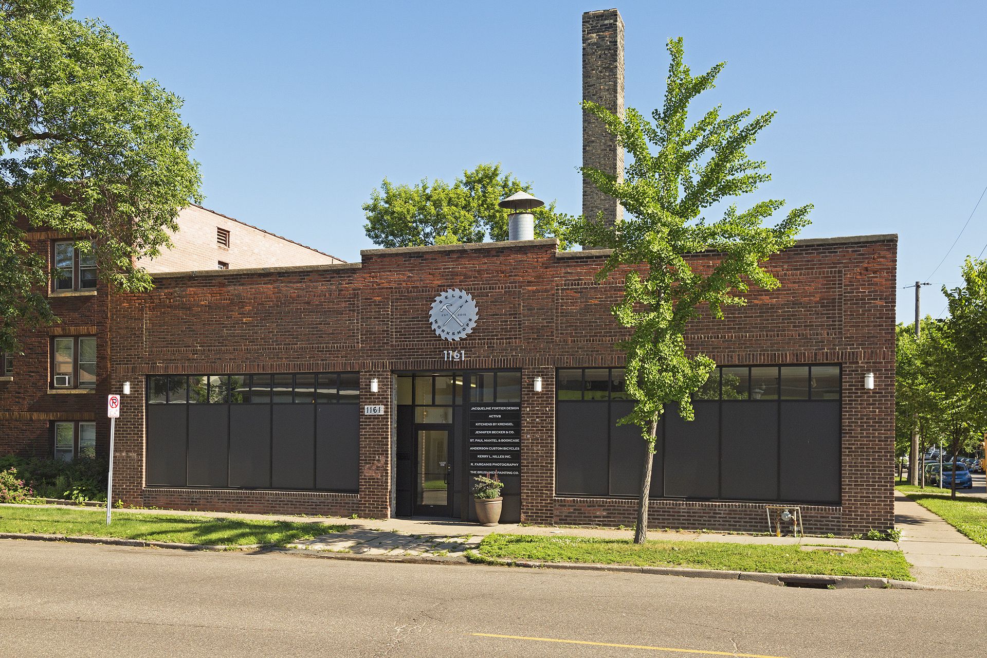 Angled view of the red brick building with a circular metal sign above its recessed glass entrance